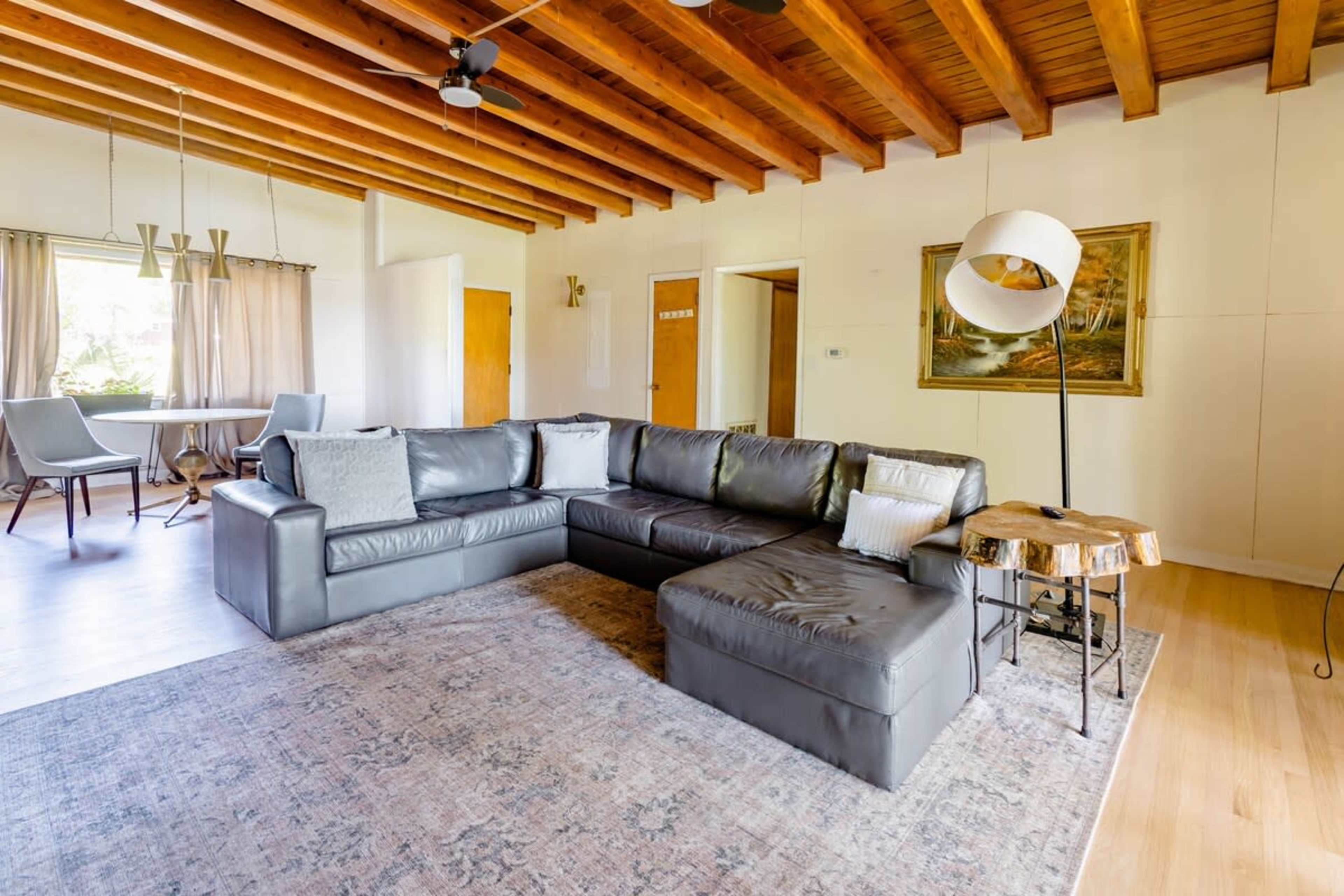 A spacious living room featuring a large leather sectional sofa, a wooden coffee table, and natural wood beam ceilings.
