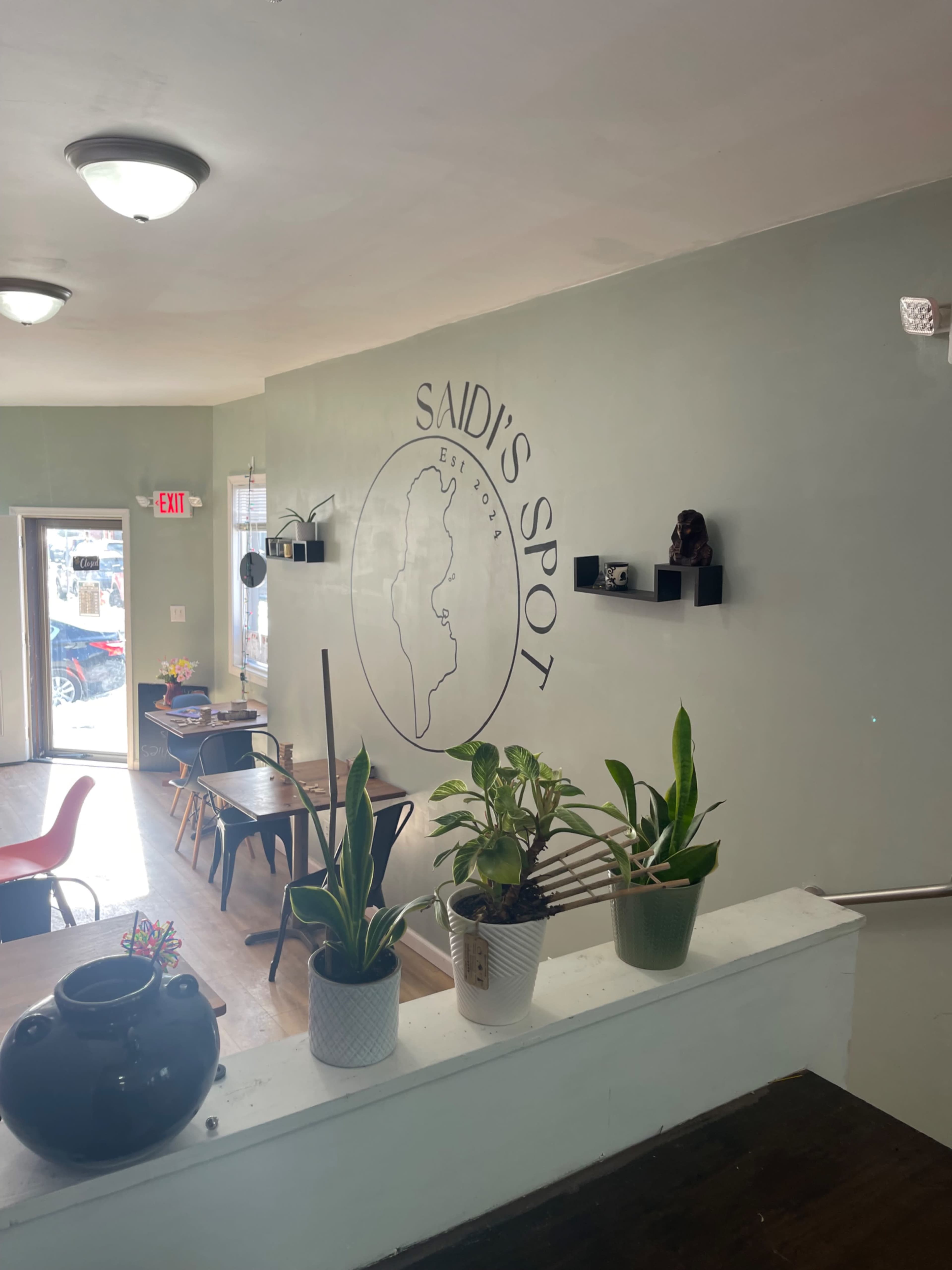 The interior of a café named "Said's Spot" features plants on a ledge, a minimalist design, and tables arranged for seating.