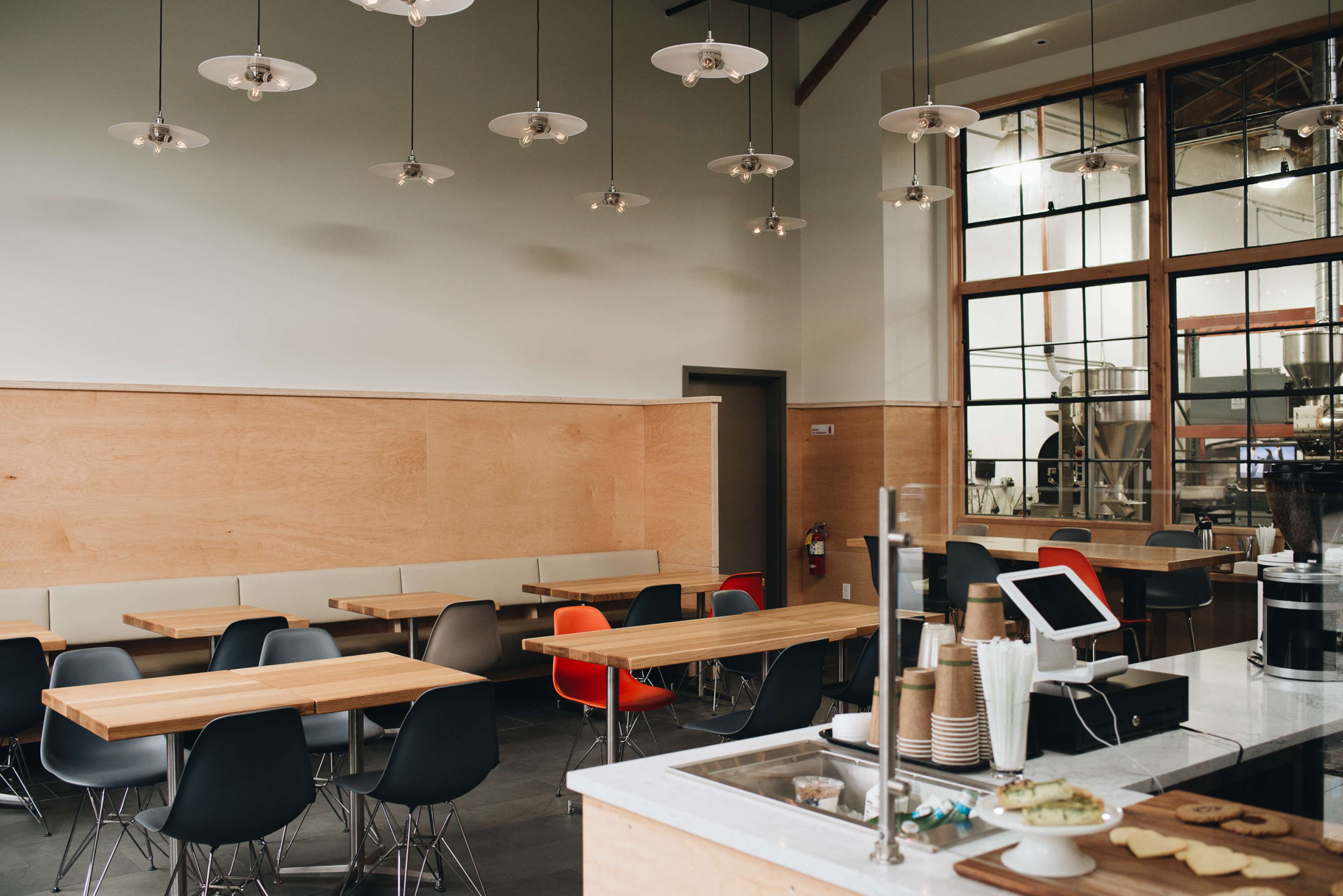 A modern café interior with wooden tables, a coffee counter, and large windows allowing natural light.