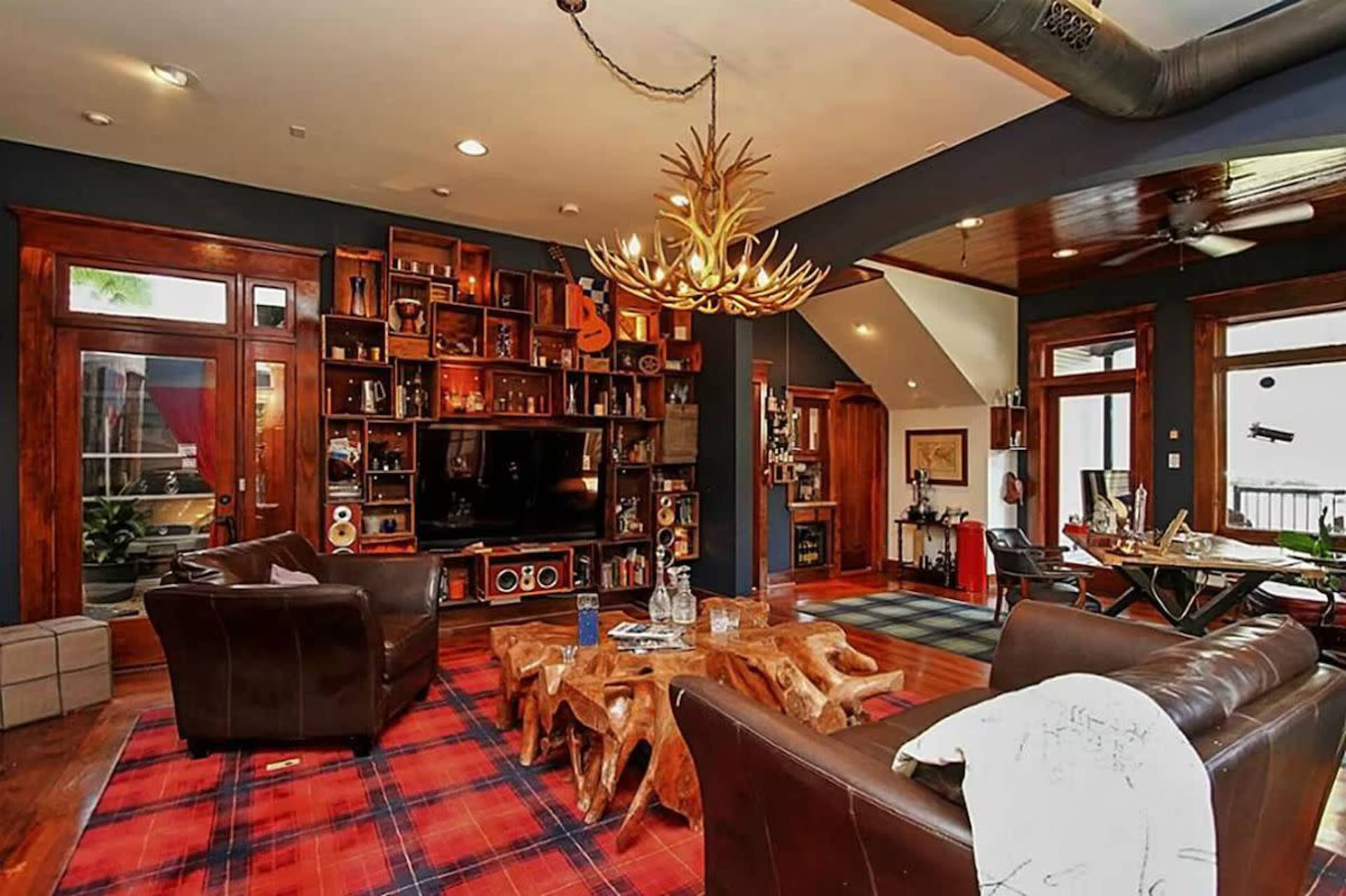 A cozy living room with leather chairs, a large wooden bookshelf, and a distinctive antler chandelier, all set on a plaid rug.