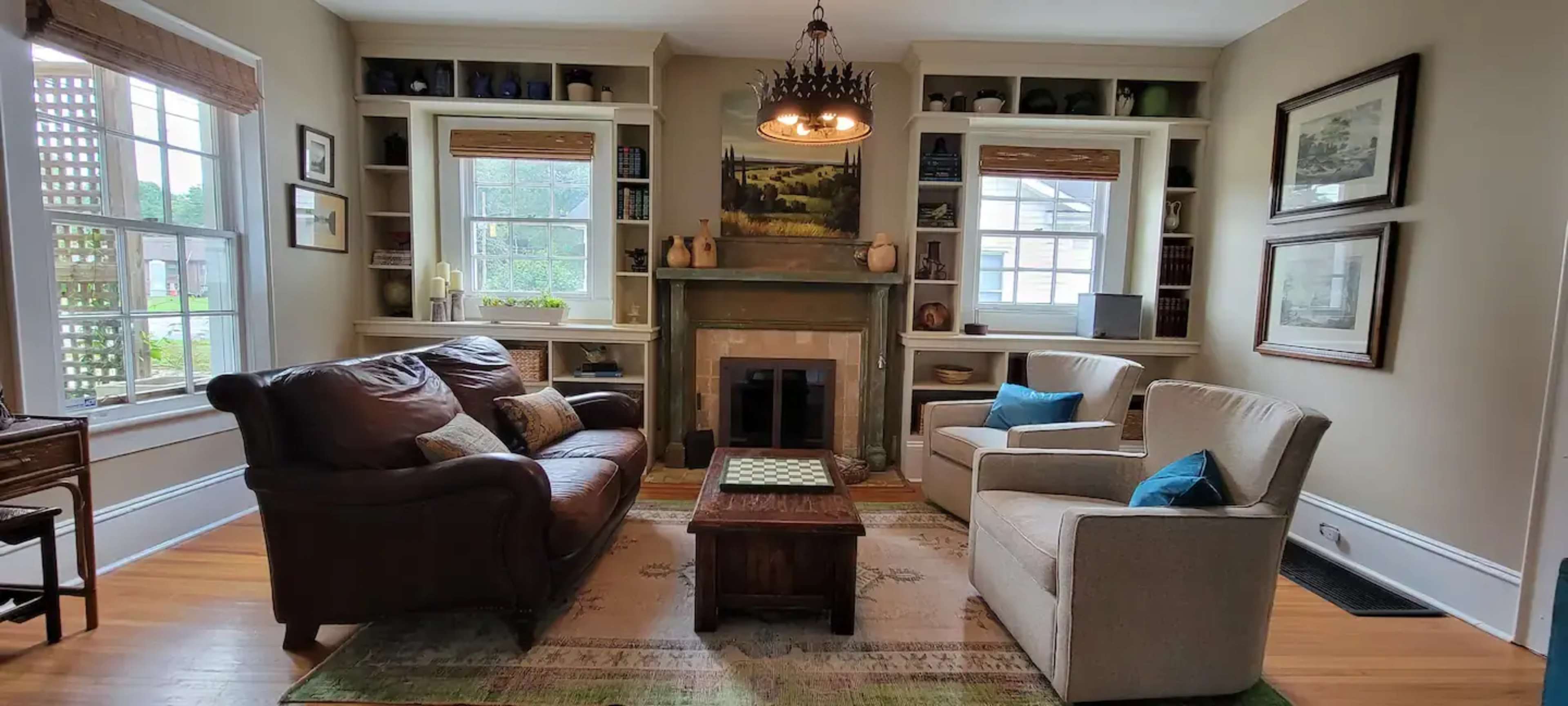 A well-furnished living room with a leather sofa, two upholstered chairs, a coffee table, and a fireplace surrounded by built-in shelves.