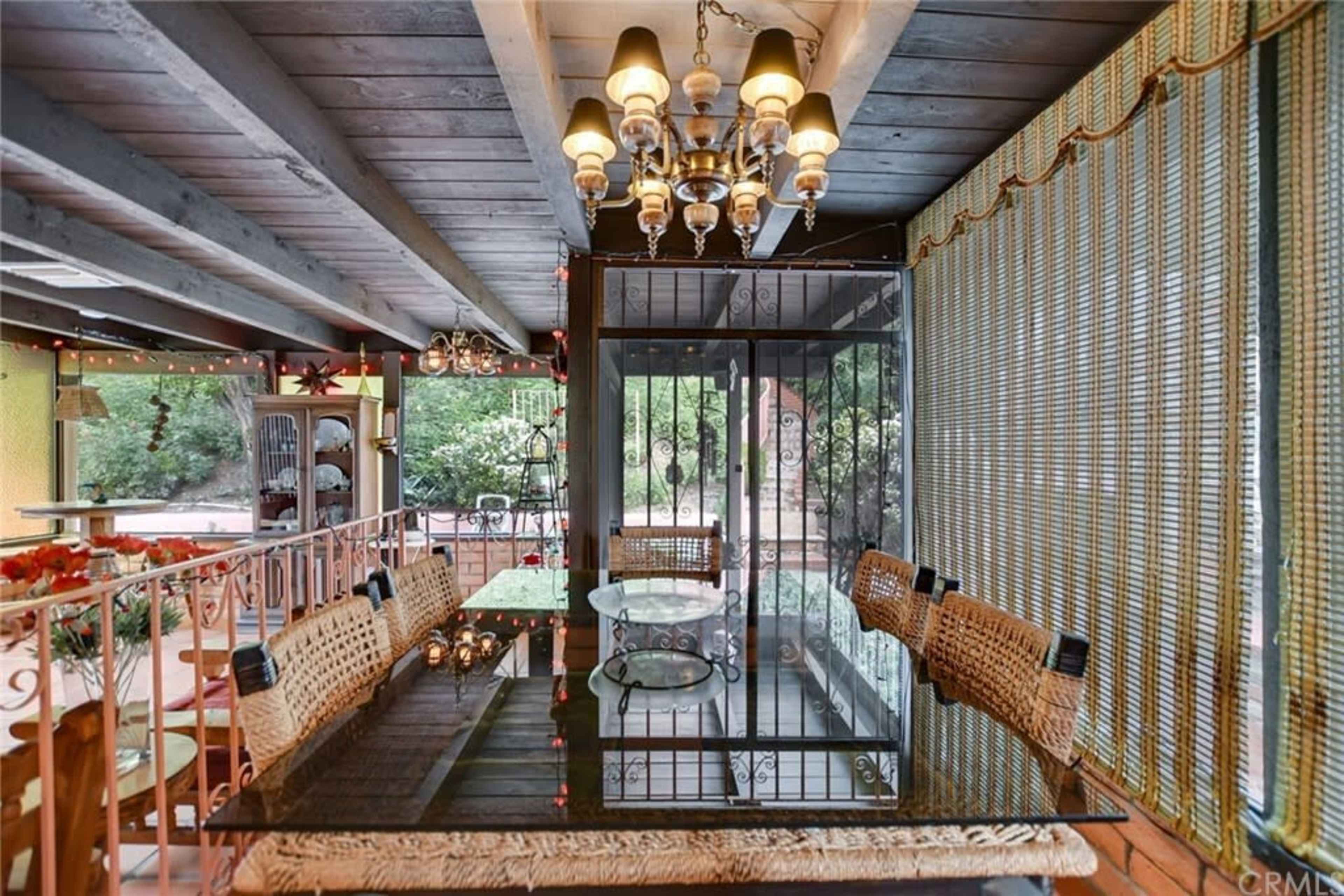The image shows a screened patio area with a long glass dining table surrounded by woven chairs and a decorative chandelier overhead.
