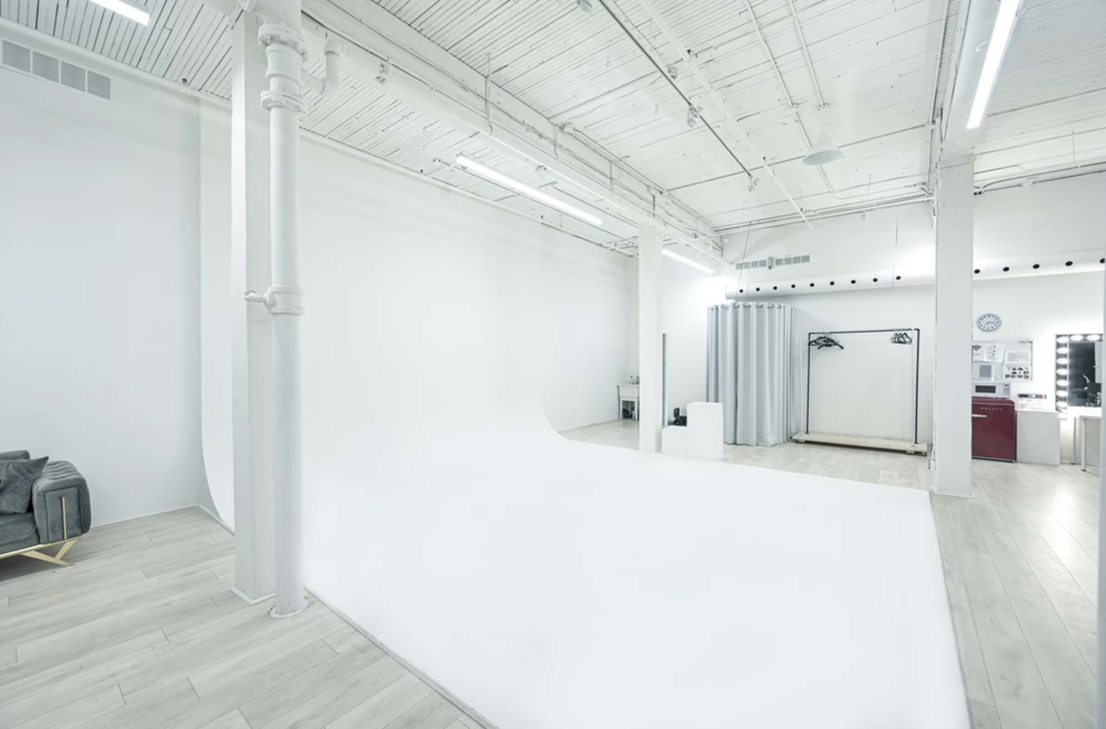 A spacious, well-lit photography studio with a large white backdrop and minimalist furnishings.
