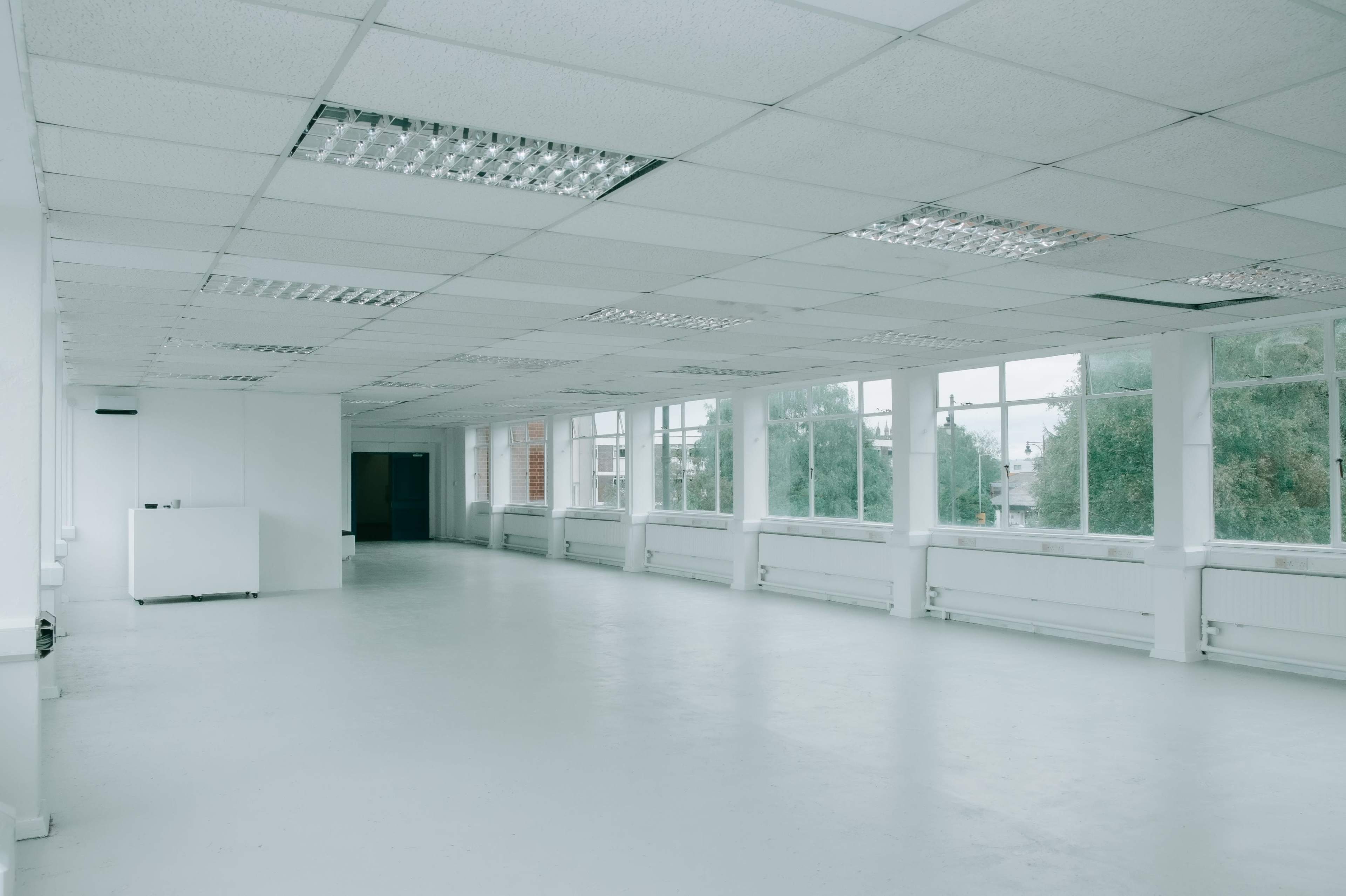A spacious, empty white room with large windows and fluorescent lighting.