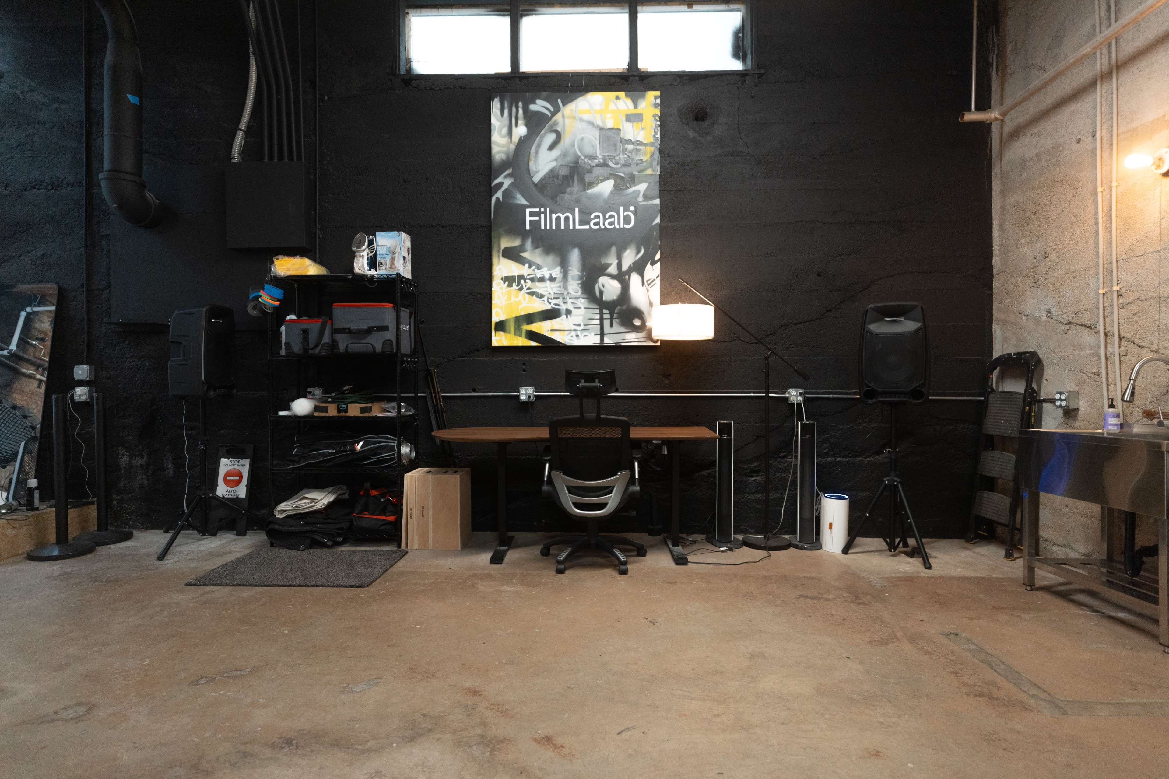 A workspace with a desk, chair, and various equipment against a black wall featuring a poster labeled "FilmLaab."