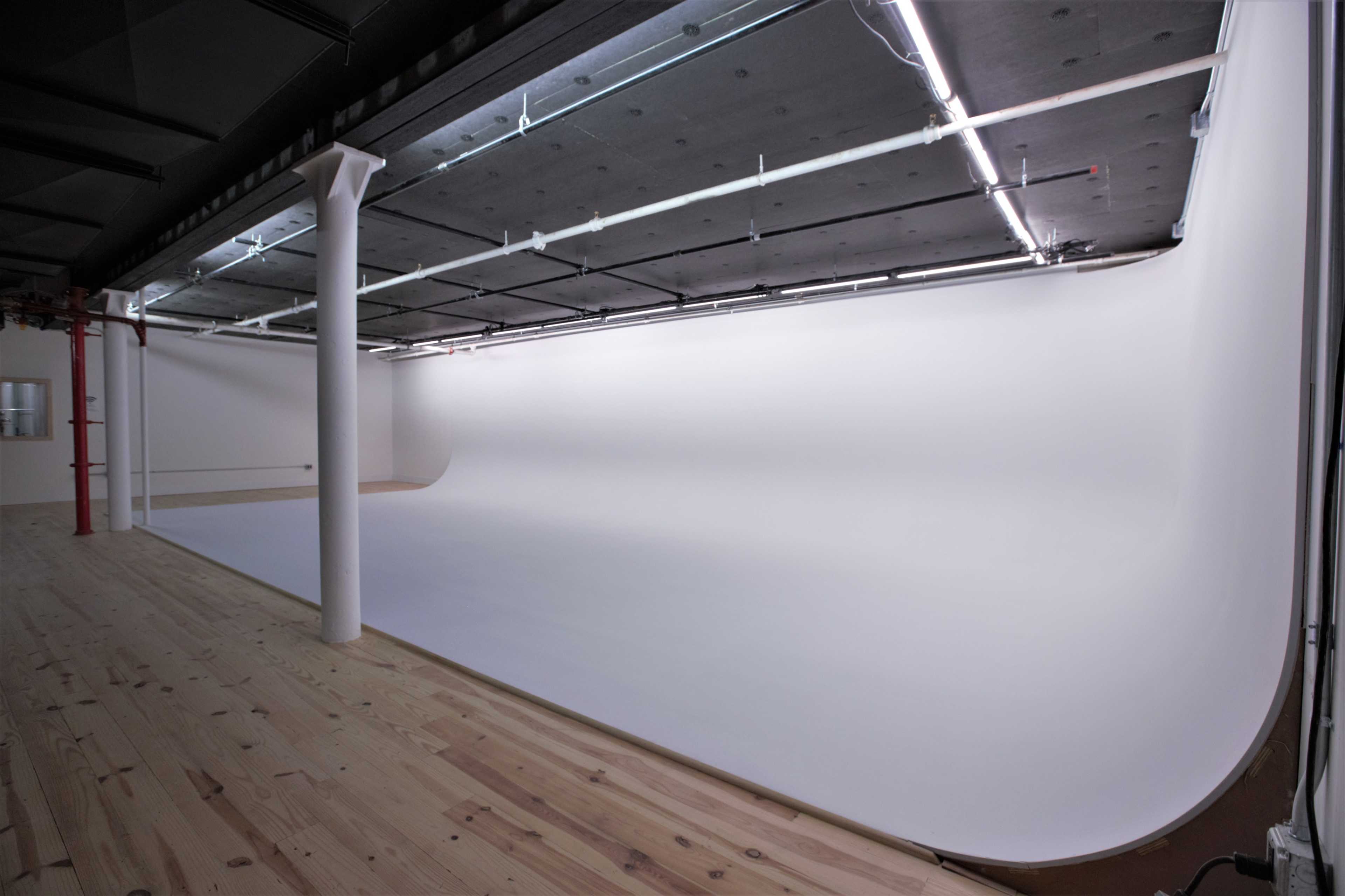 A spacious photography studio with a seamless white backdrop and wooden flooring.