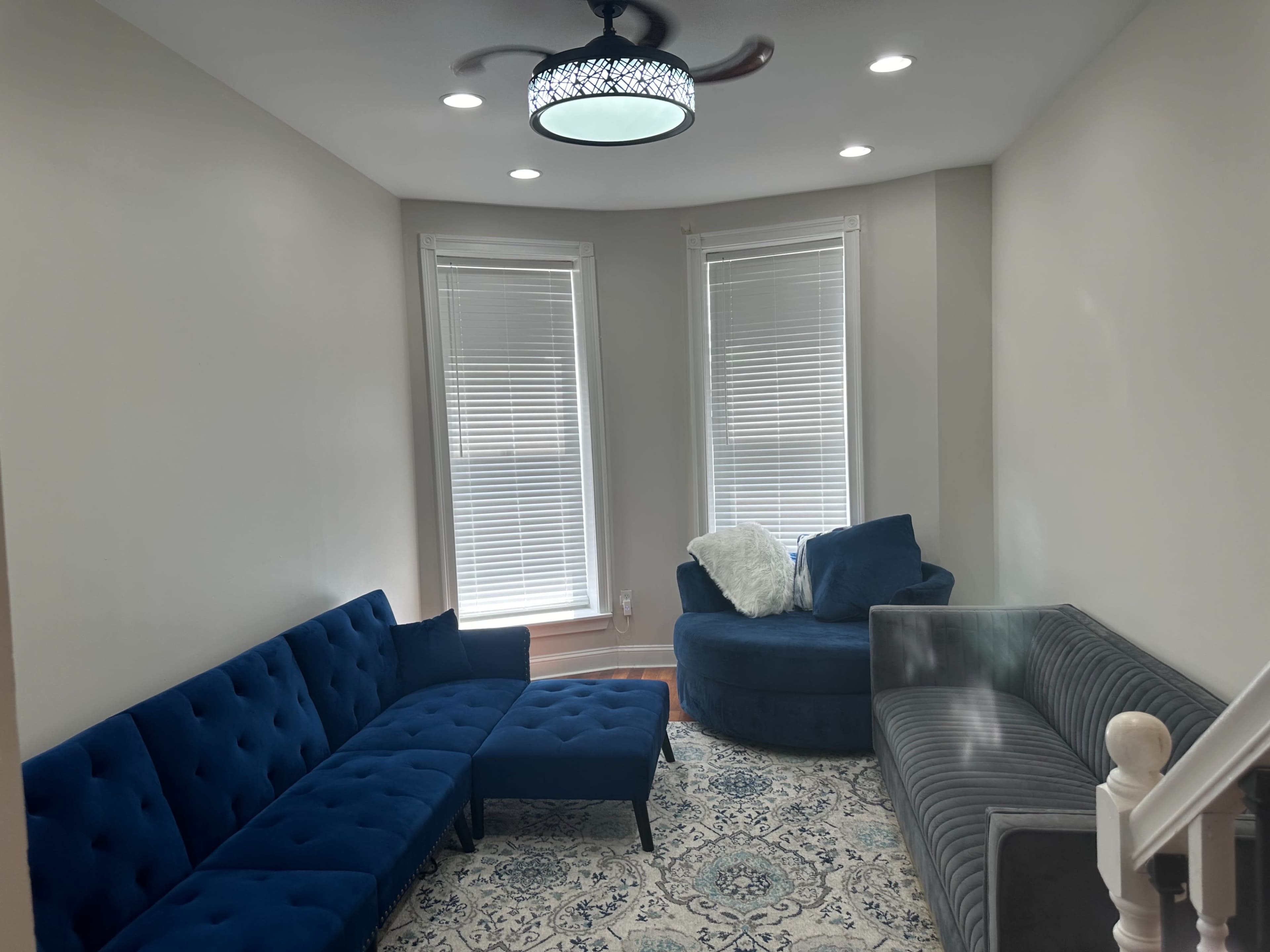 A living room featuring a blue velvet sectional sofa, a circular chair, and a decorative area rug, illuminated by a modern ceiling light fixture.