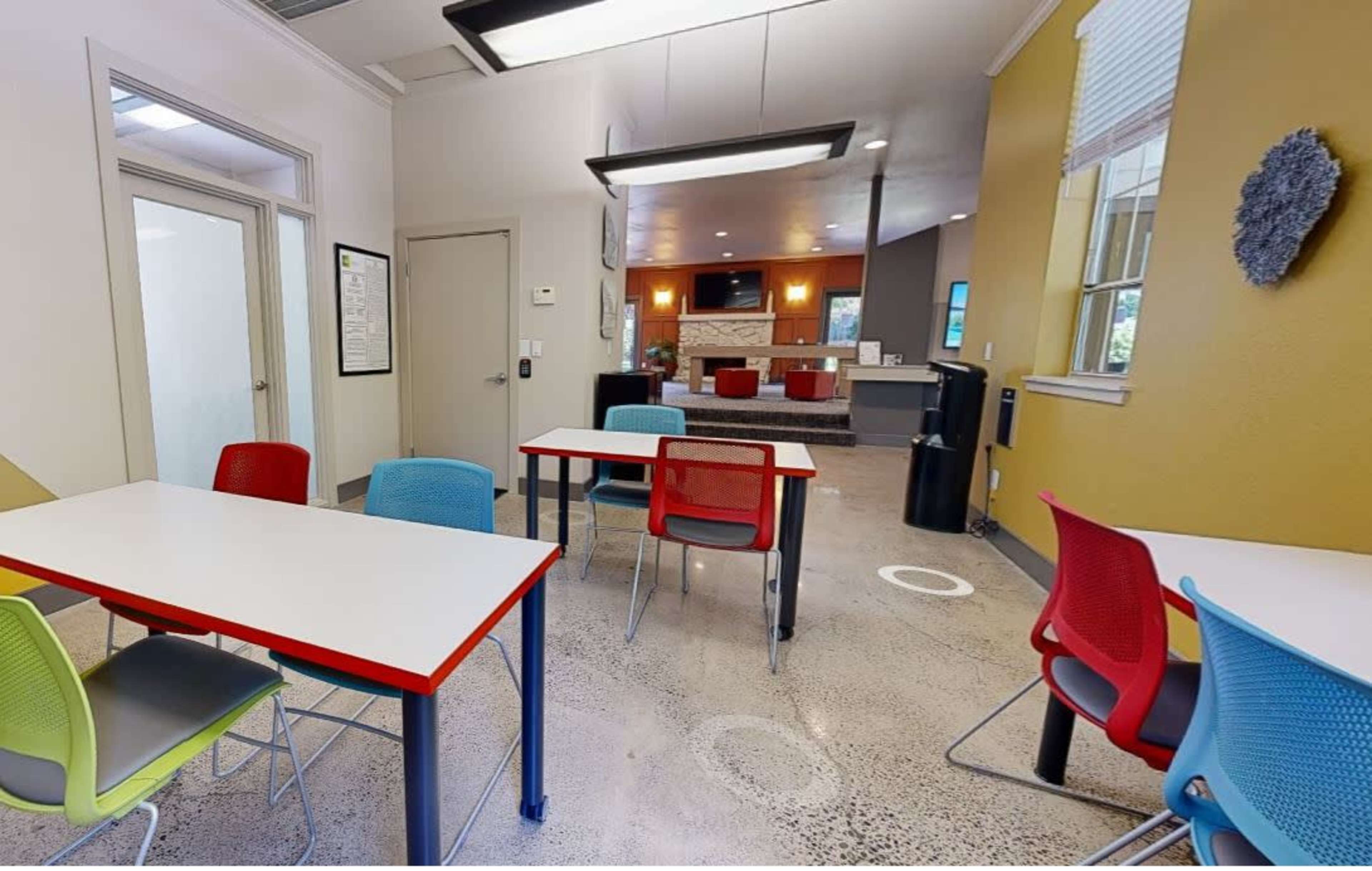 A well-lit room featuring several tables with colorful chairs arranged on a polished concrete floor.