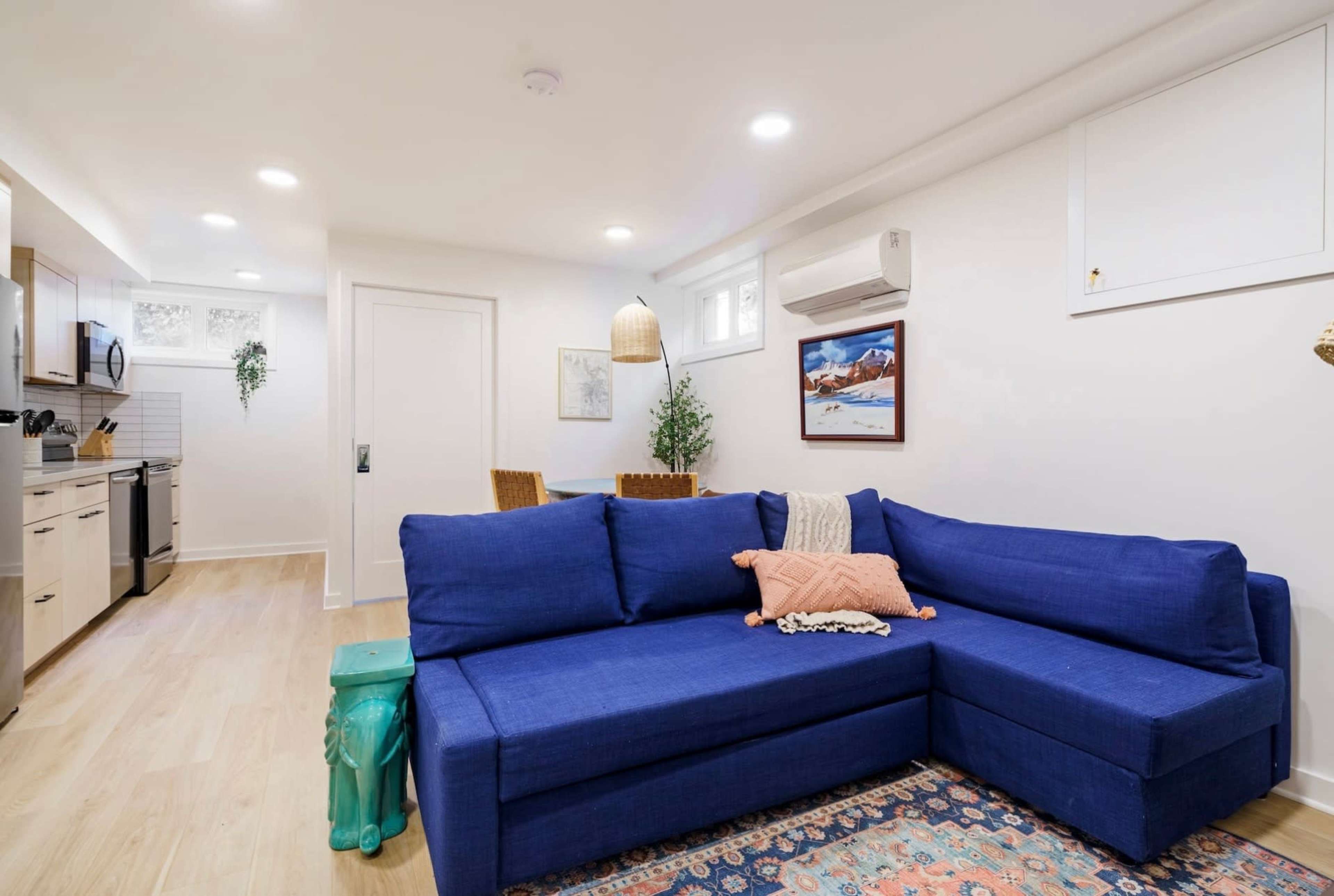 A modern living area with a blue sectional sofa, a small dining table, and a kitchen in a well-lit, open layout.