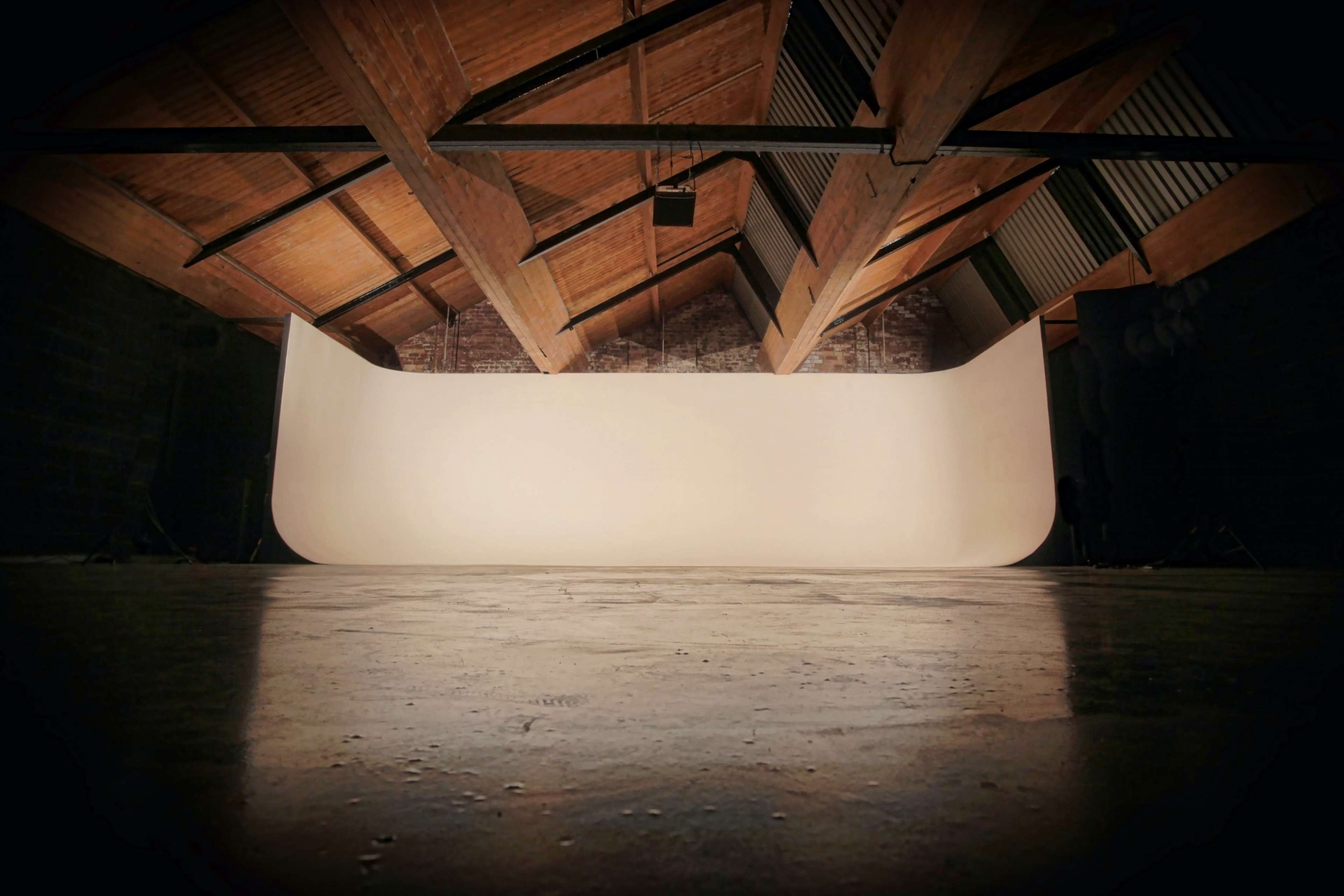 A spacious, empty studio with a curved backdrop and wooden beams overhead.
