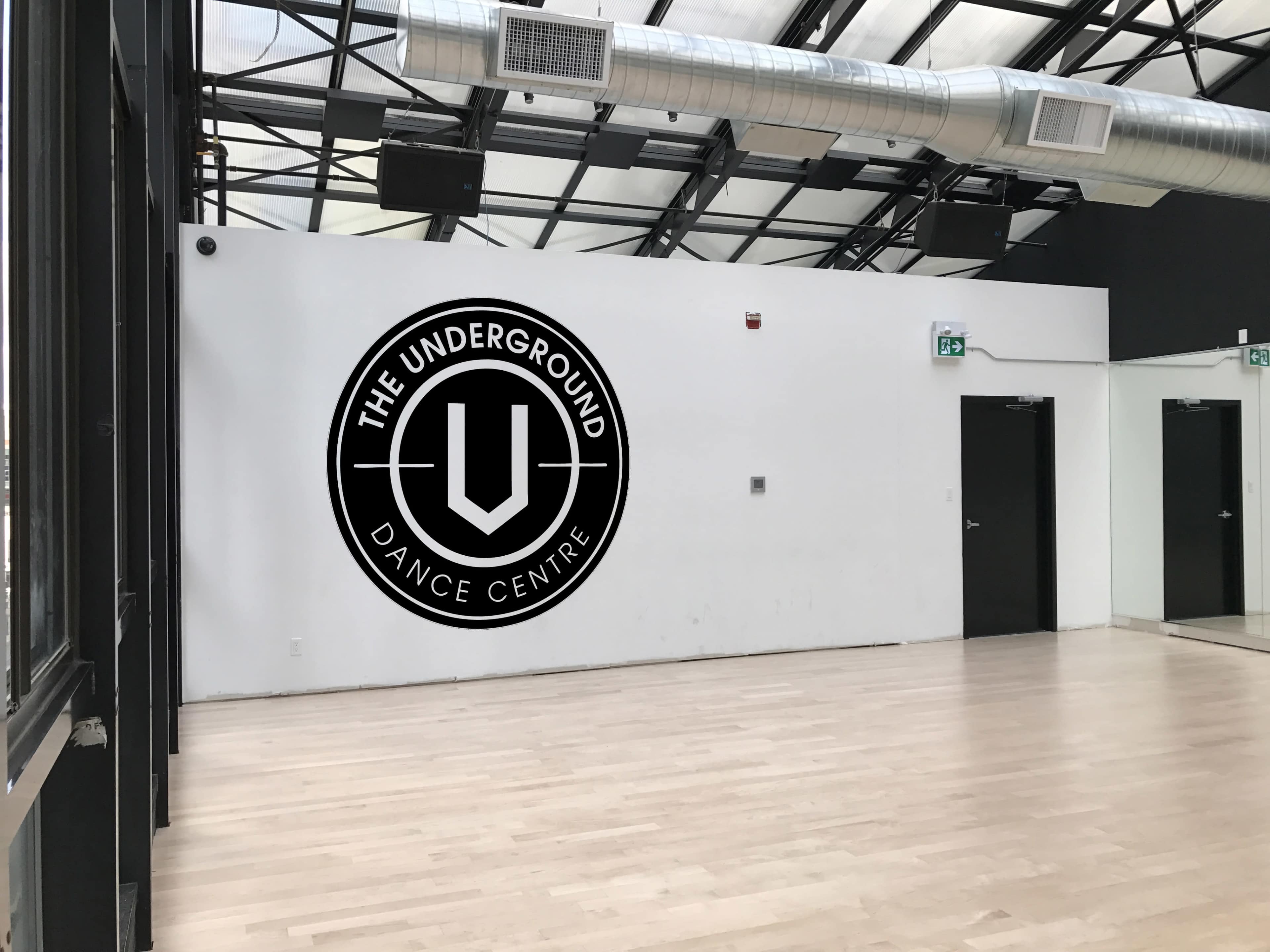 The image shows a dance studio with a wooden floor and a wall featuring the logo of "The Underground Dance Centre."