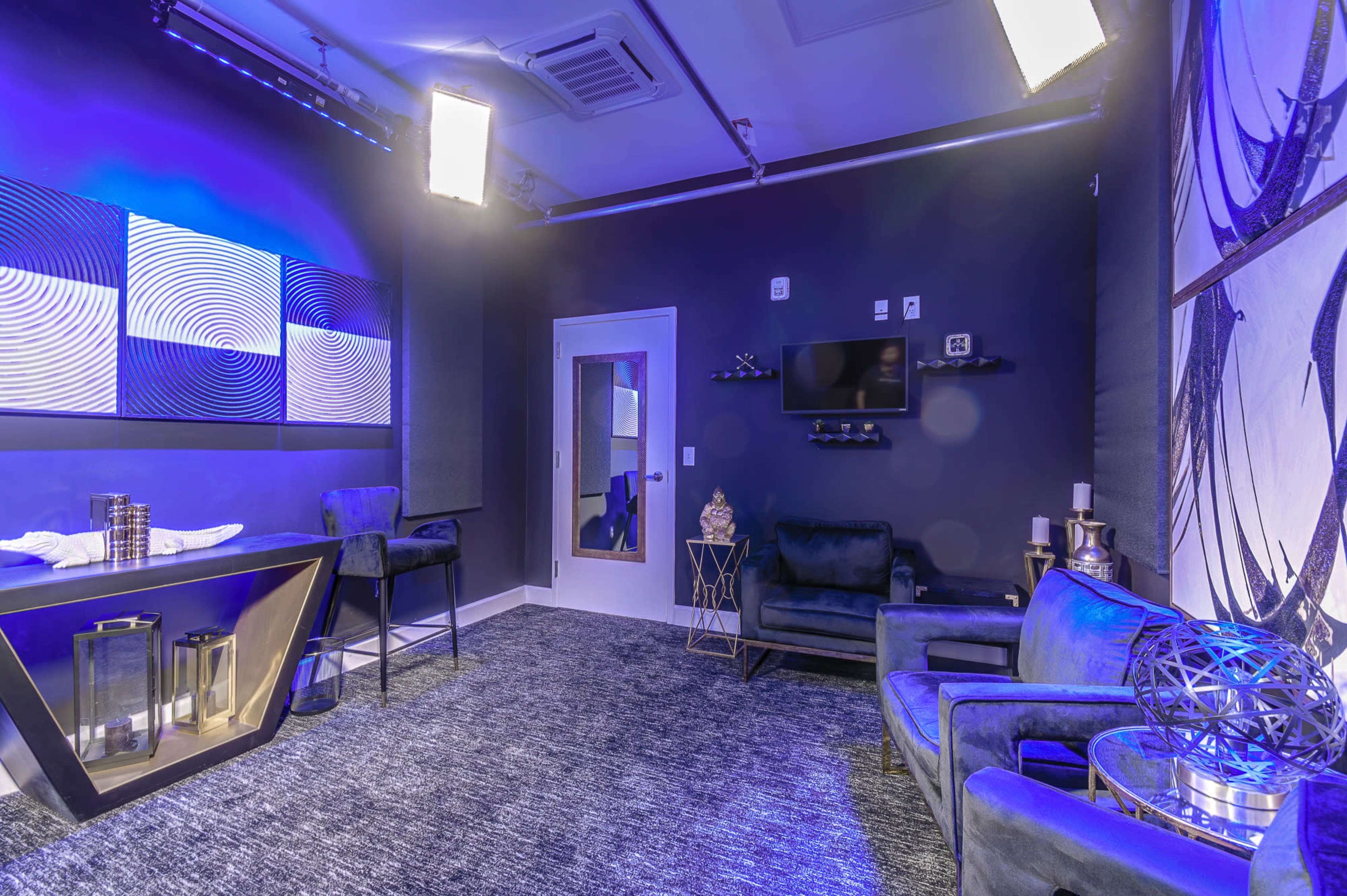 The image shows a modern, stylish studio room featuring a dark blue color scheme, two chairs, and a television on the wall.