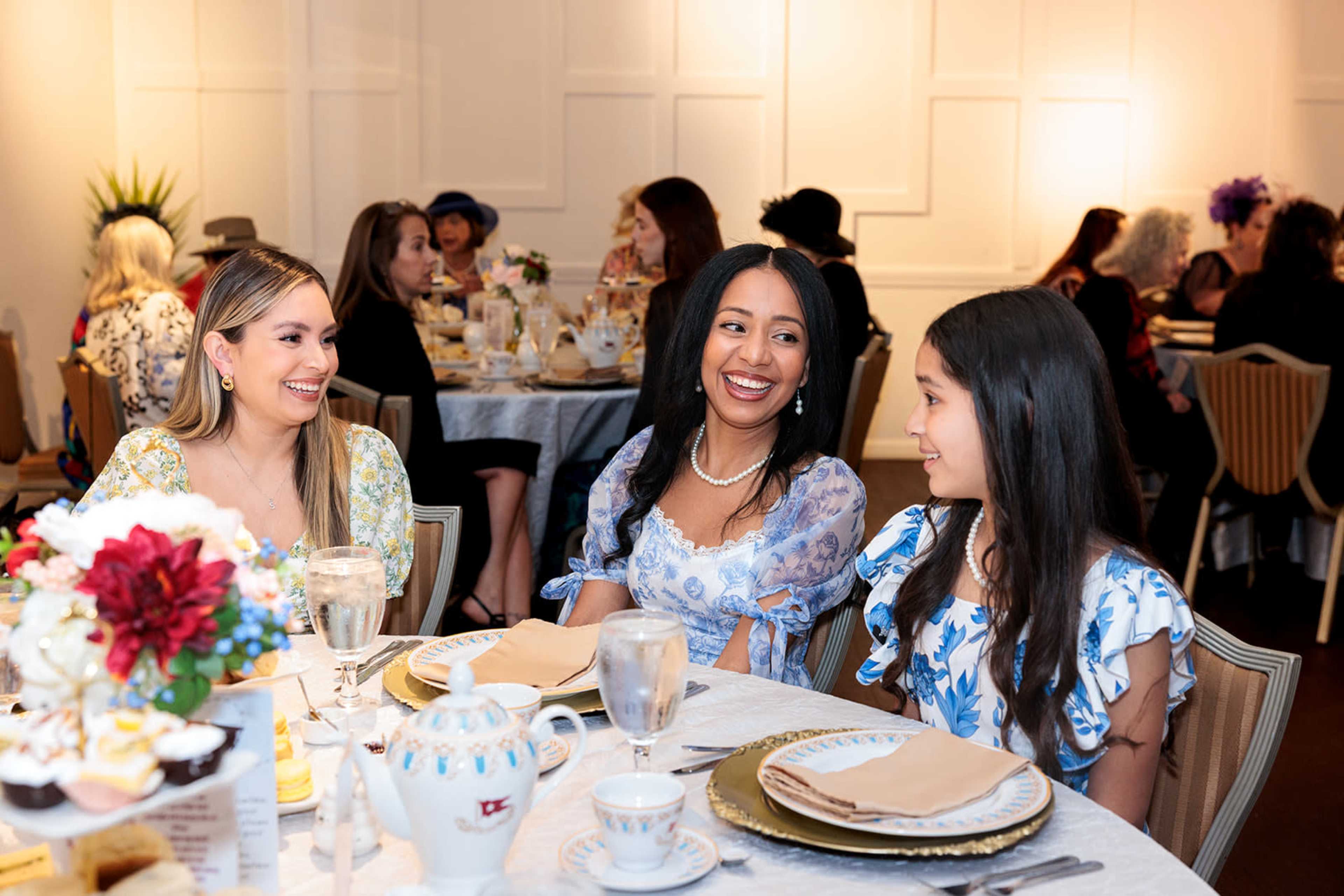 Three women sit at a elegantly set dining table, sharing smiles and conversation during a social event.