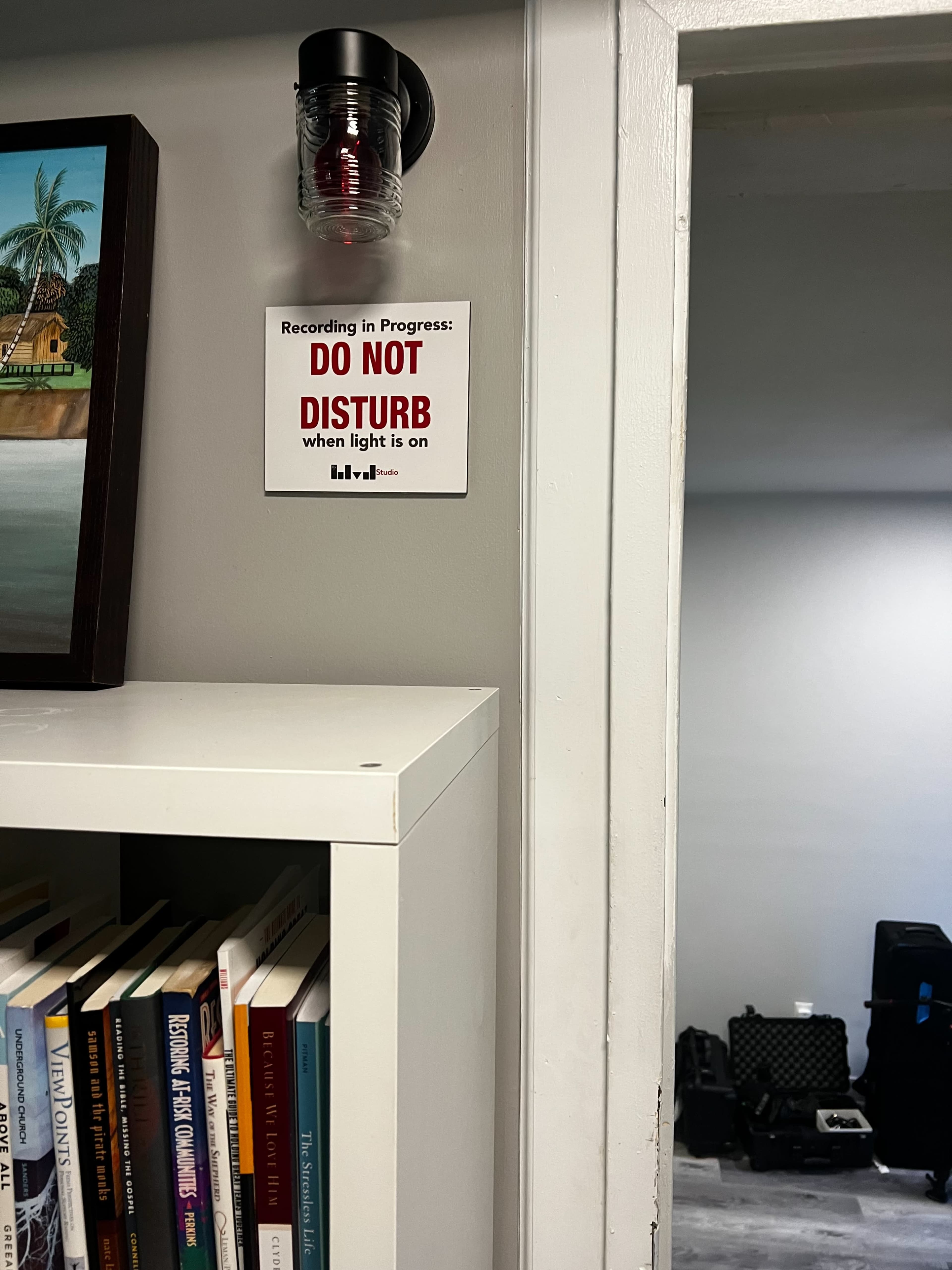 A sign that reads "Recording in Progress: DO NOT DISTURB when light is on" is mounted on a wall near a shelf filled with books.