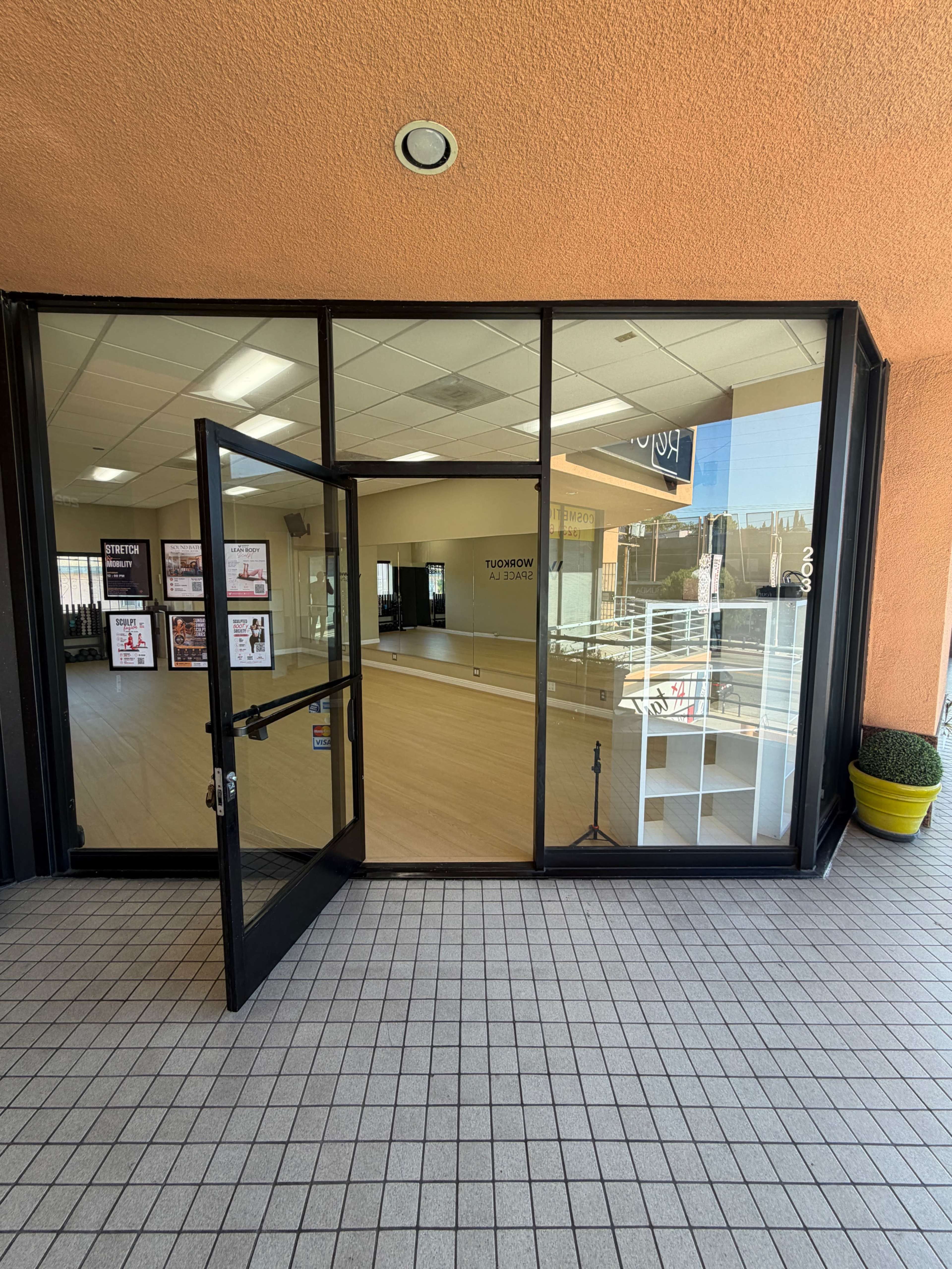 The image shows the entrance of a commercial building with large glass doors opening into a spacious, well-lit interior featuring a wooden floor.
