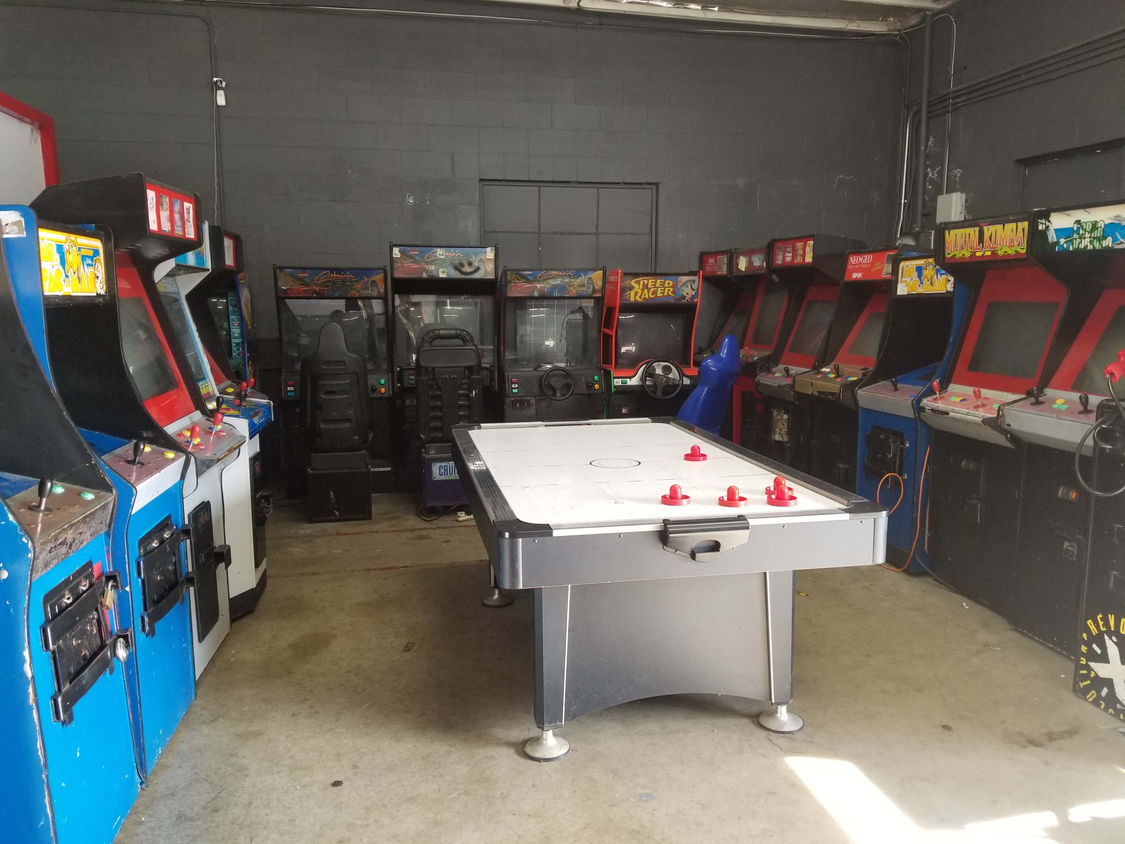 A room filled with various arcade game machines lining the walls, with a central air hockey table.
