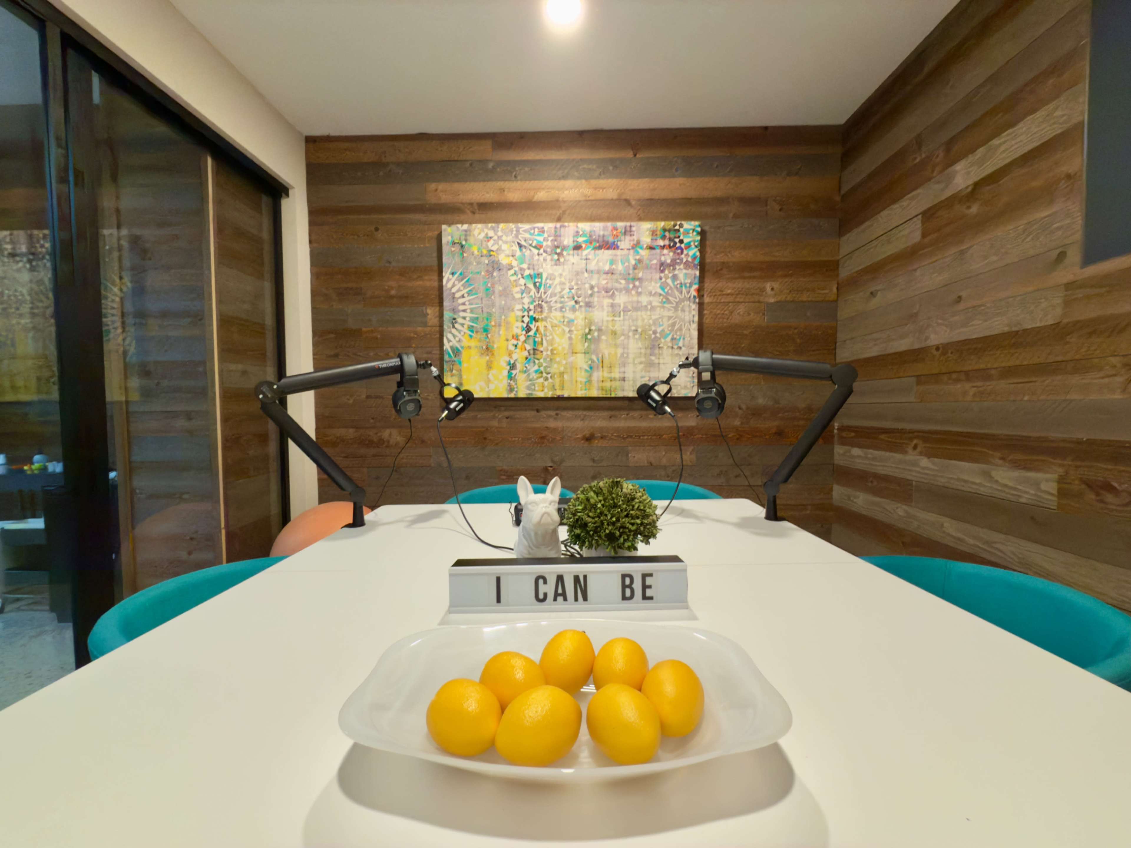 A modern meeting room features a white table with a plate of lemons, framed by wood-paneled walls and artistic decor.
