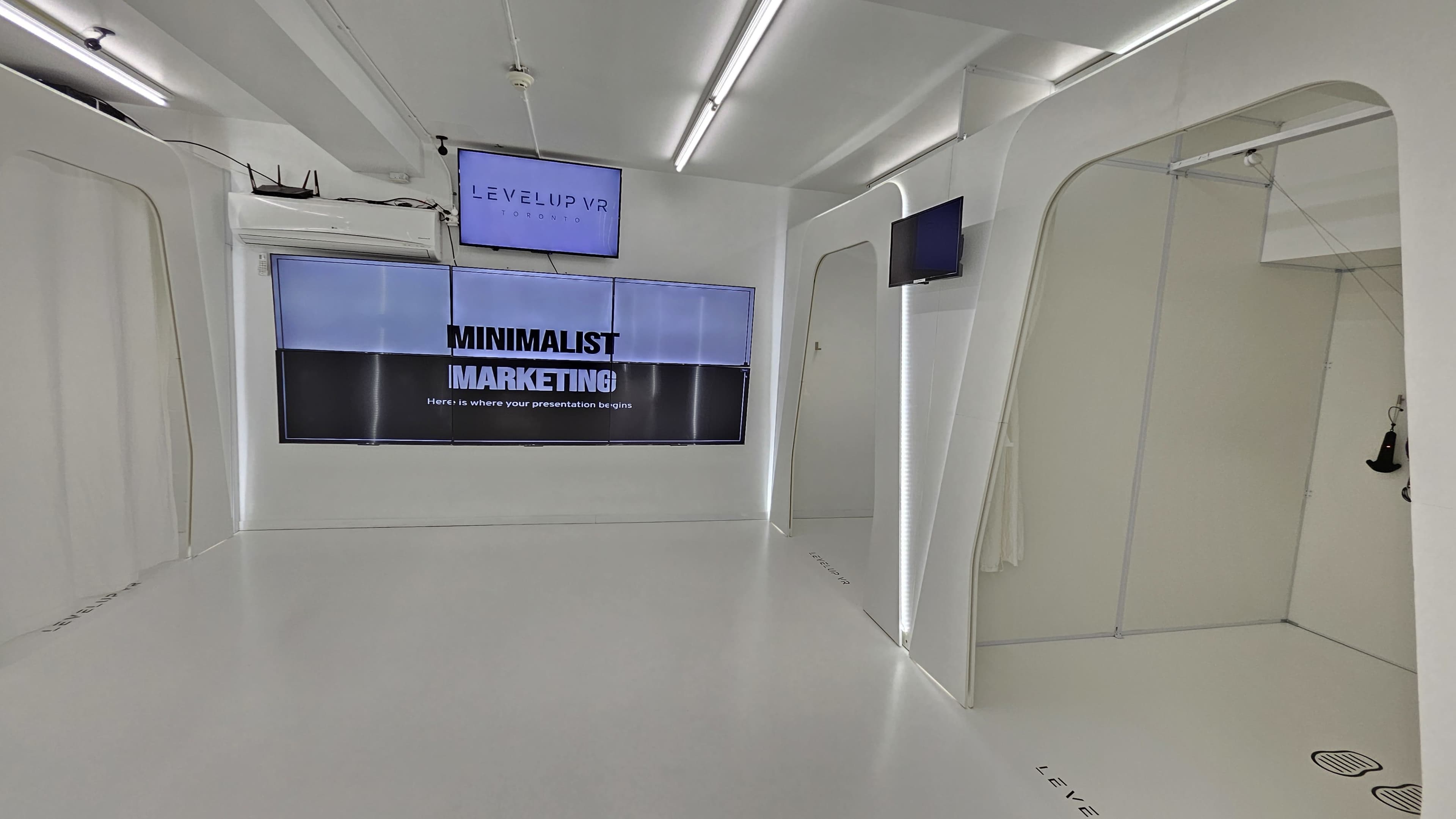 The image depicts a modern, minimalistic marketing space featuring white walls, a large window with the text "MINIMALIST MARKETING," and digital screens.