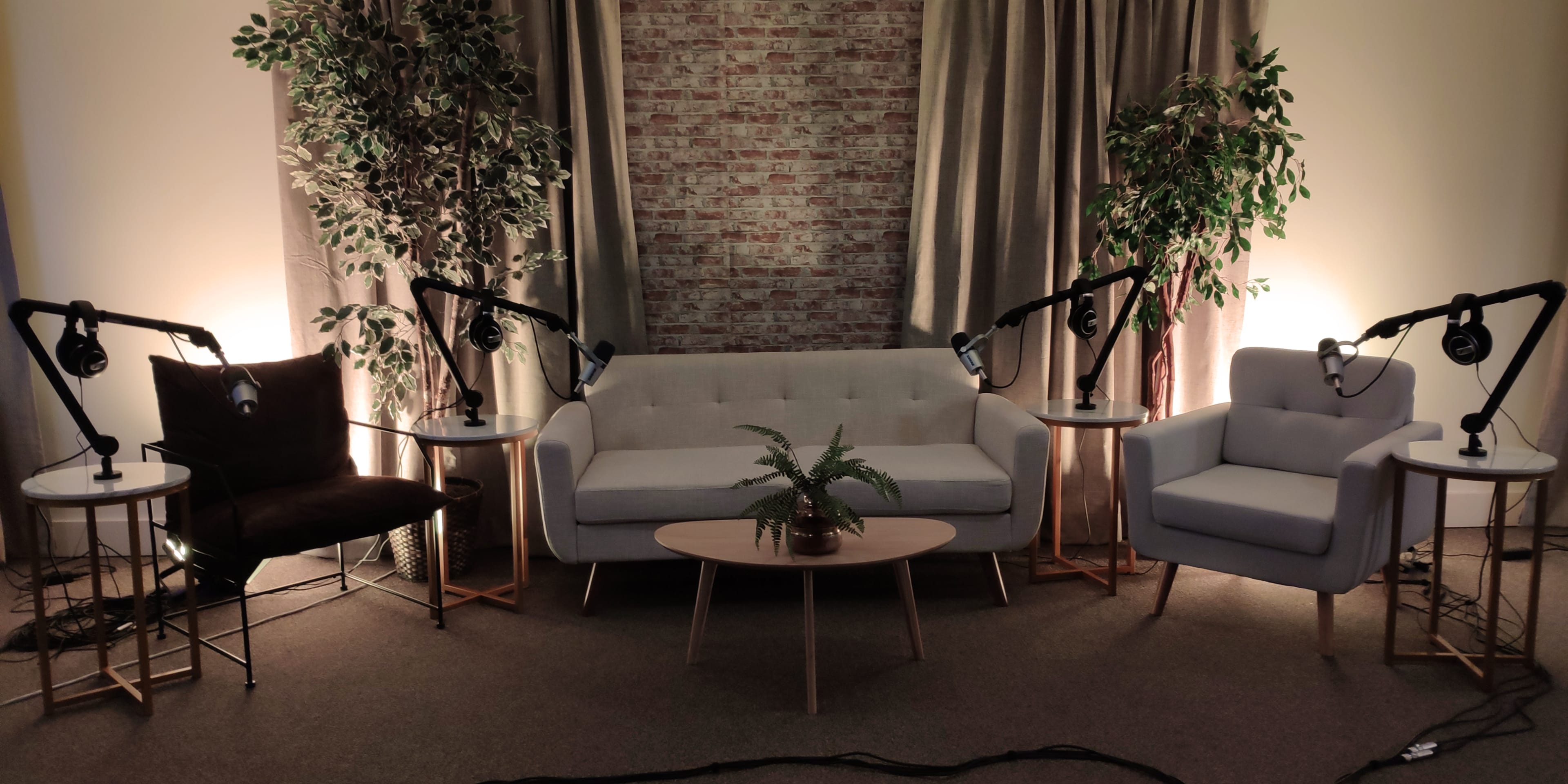 A cozy seating area with two armchairs and a sofa, surrounded by potted plants and equipped with studio microphones on stands.