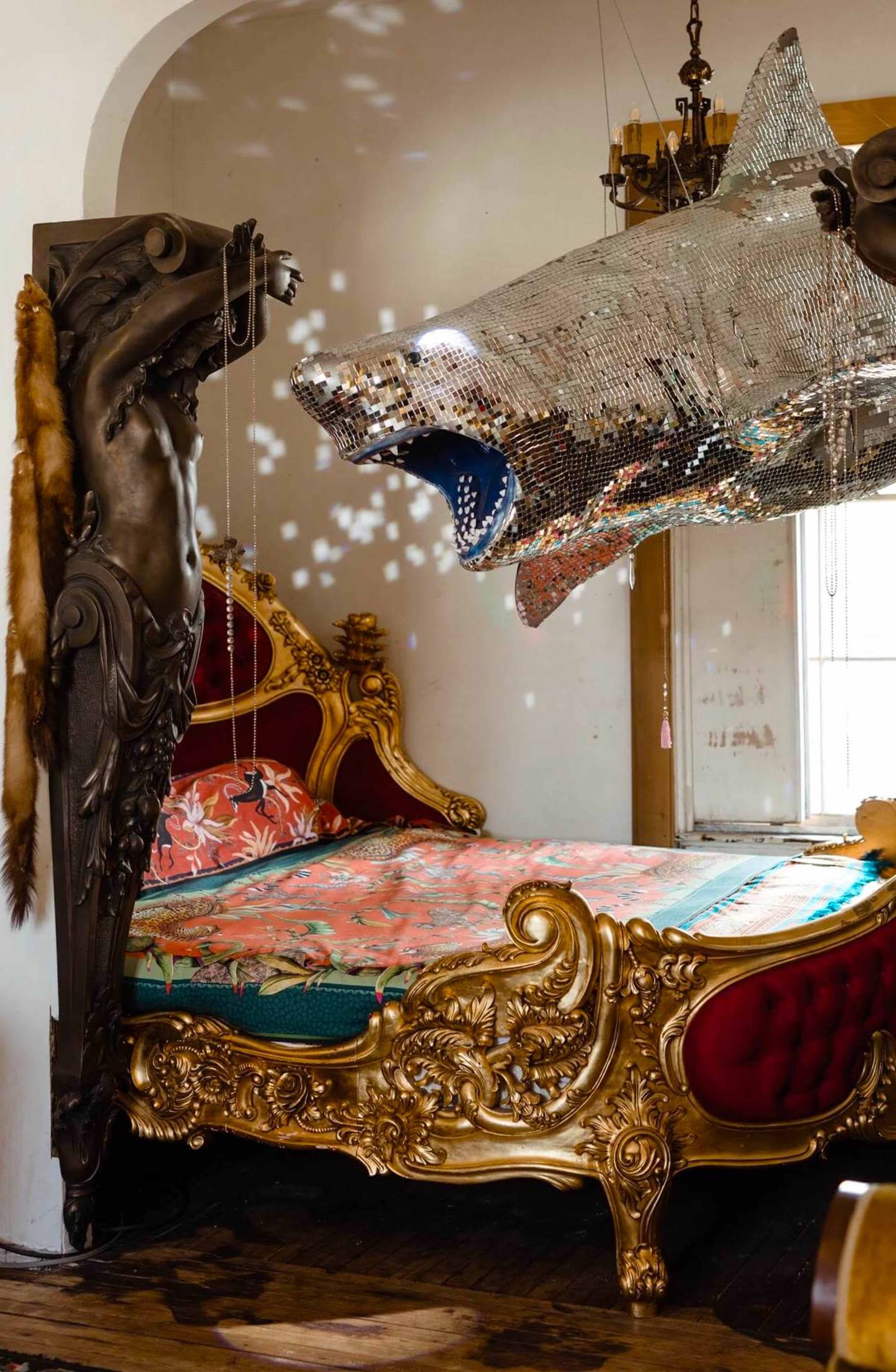 An ornate bedroom with a lavishly decorated bed and a large, silver disco ball shaped like a shark hanging from the ceiling.