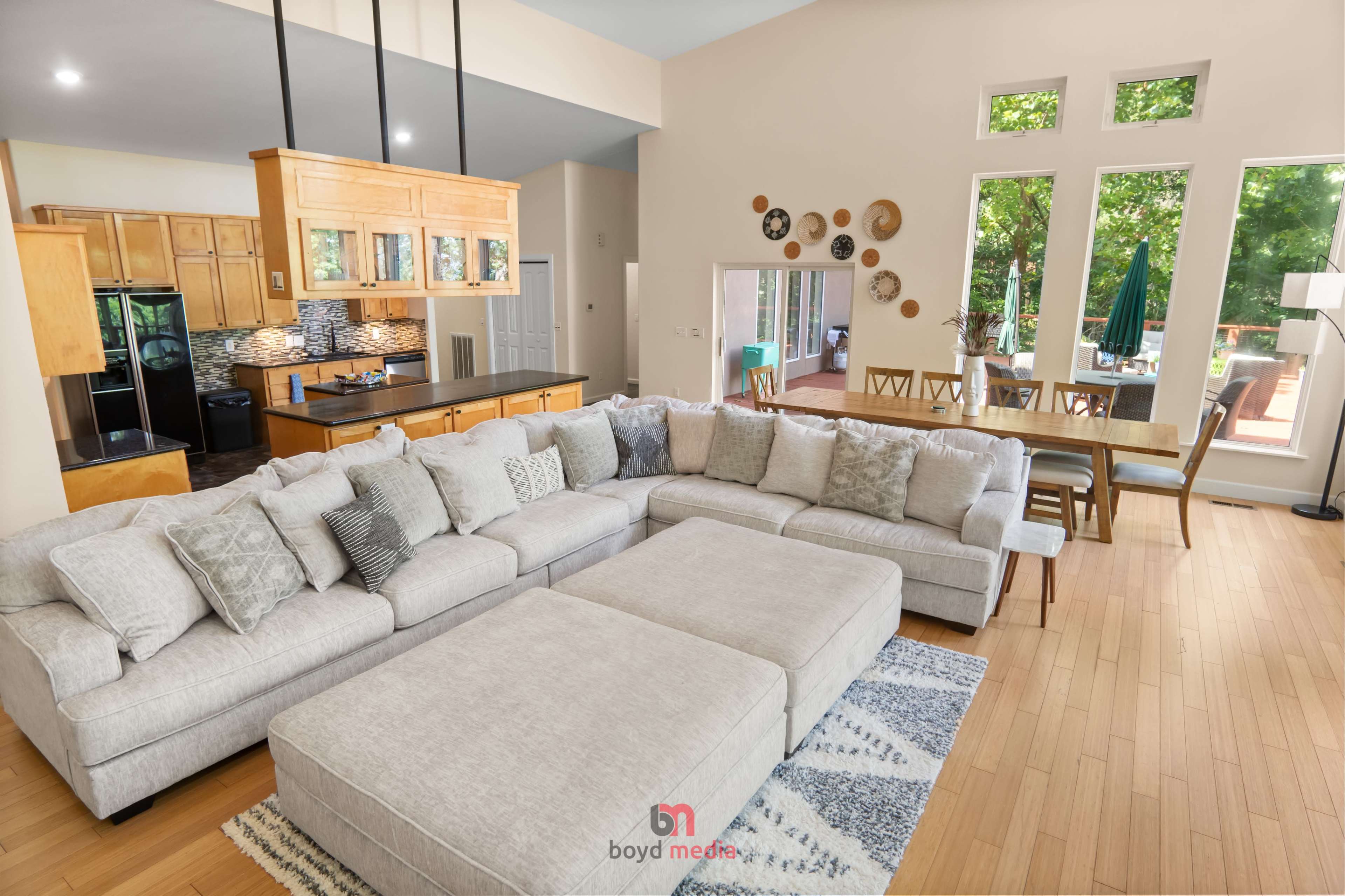 A spacious living room features a large sectional sofa, a dining area with a table, and large windows allowing natural light to fill the space.