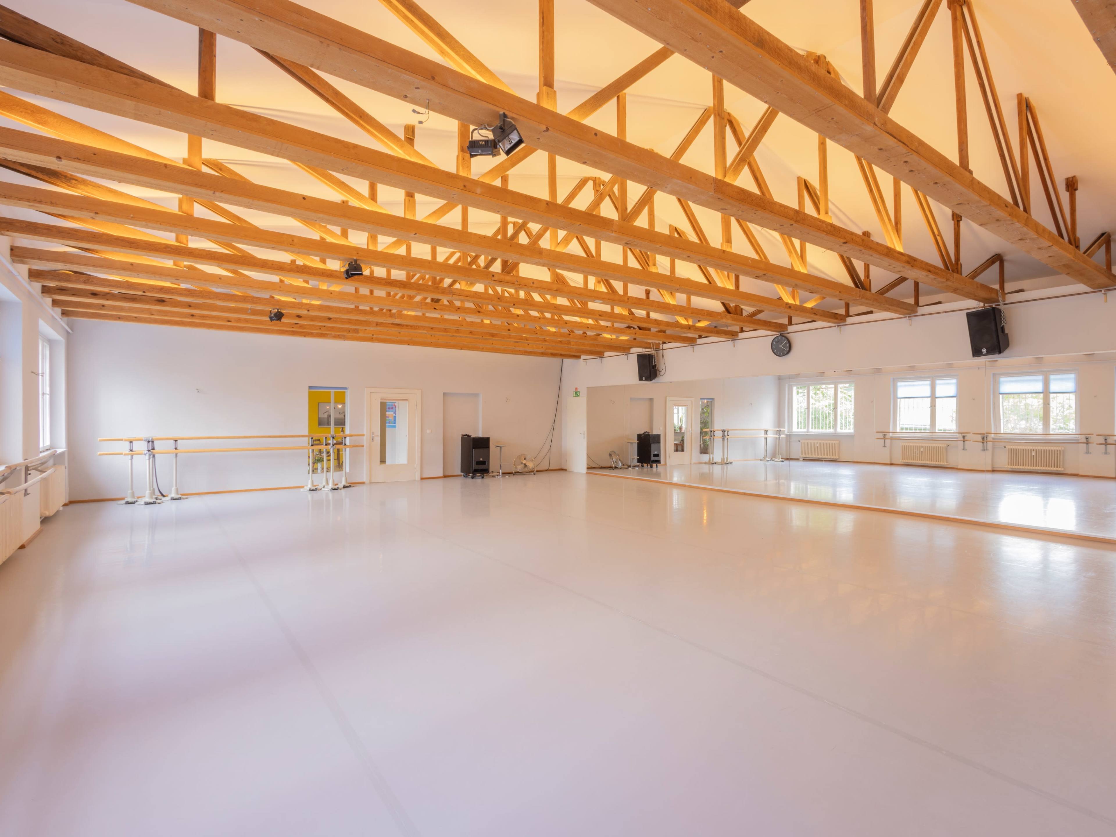 The image shows a spacious dance studio with wooden beams, mirrors, and ballet bars along the walls.