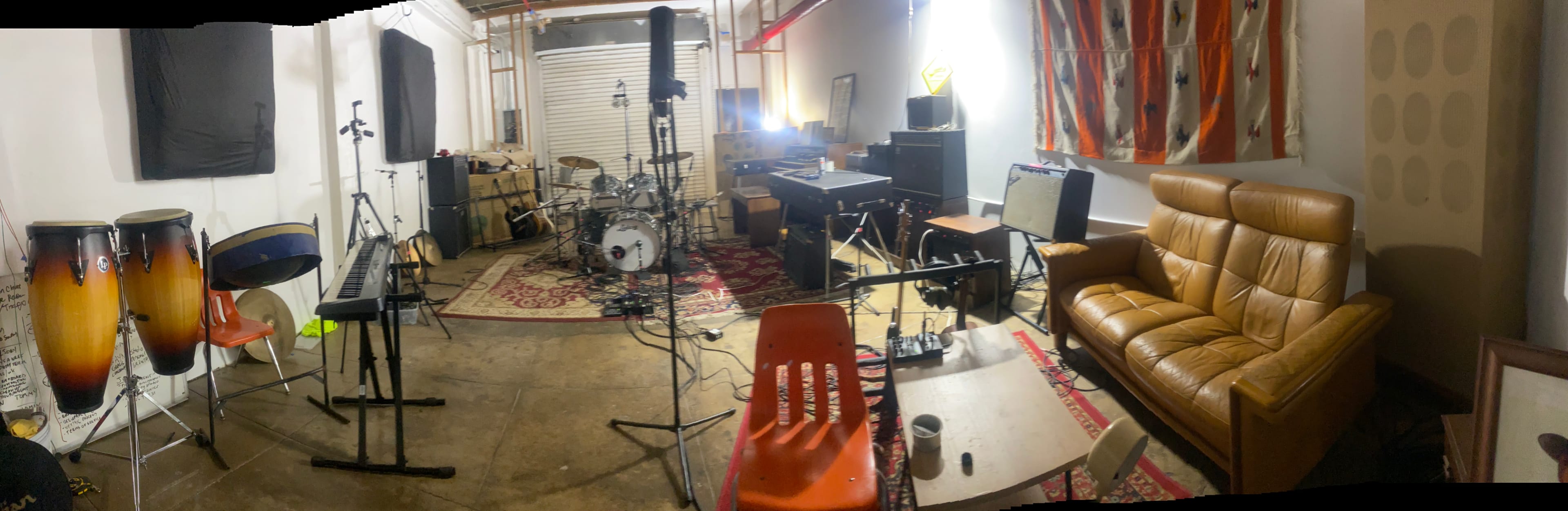 The image shows a music studio with various instruments, including drums, keyboards, and amplifiers, alongside a couch and chairs.