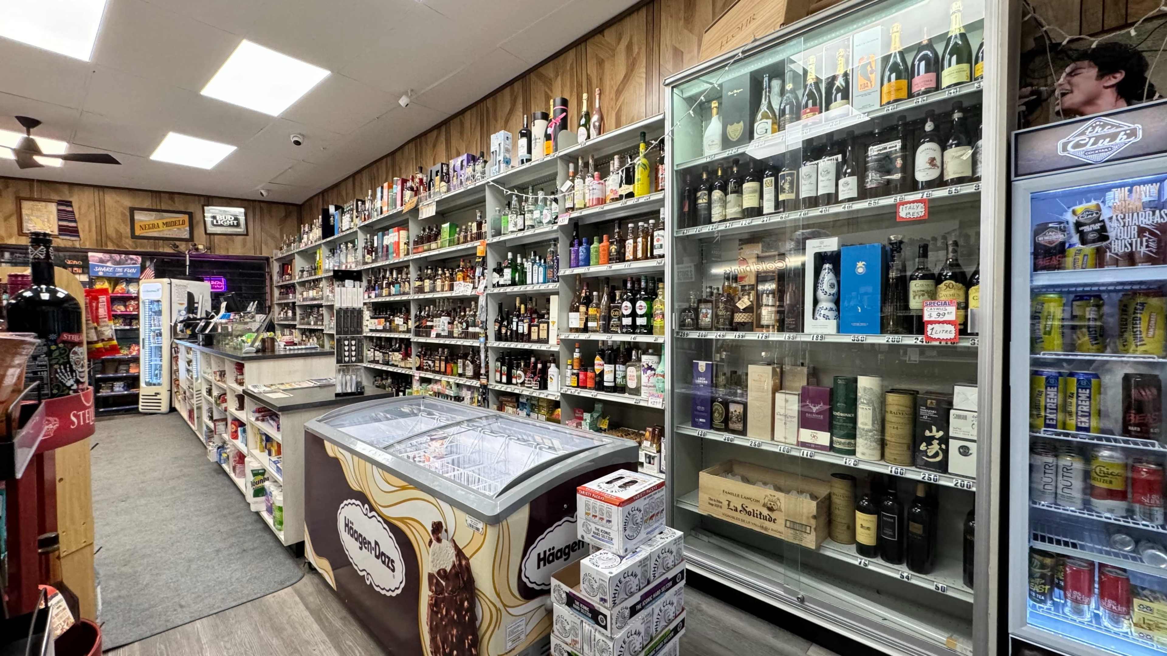 The image shows the interior of a liquor store with shelves filled with various alcoholic beverages and a refrigeration unit at the center.