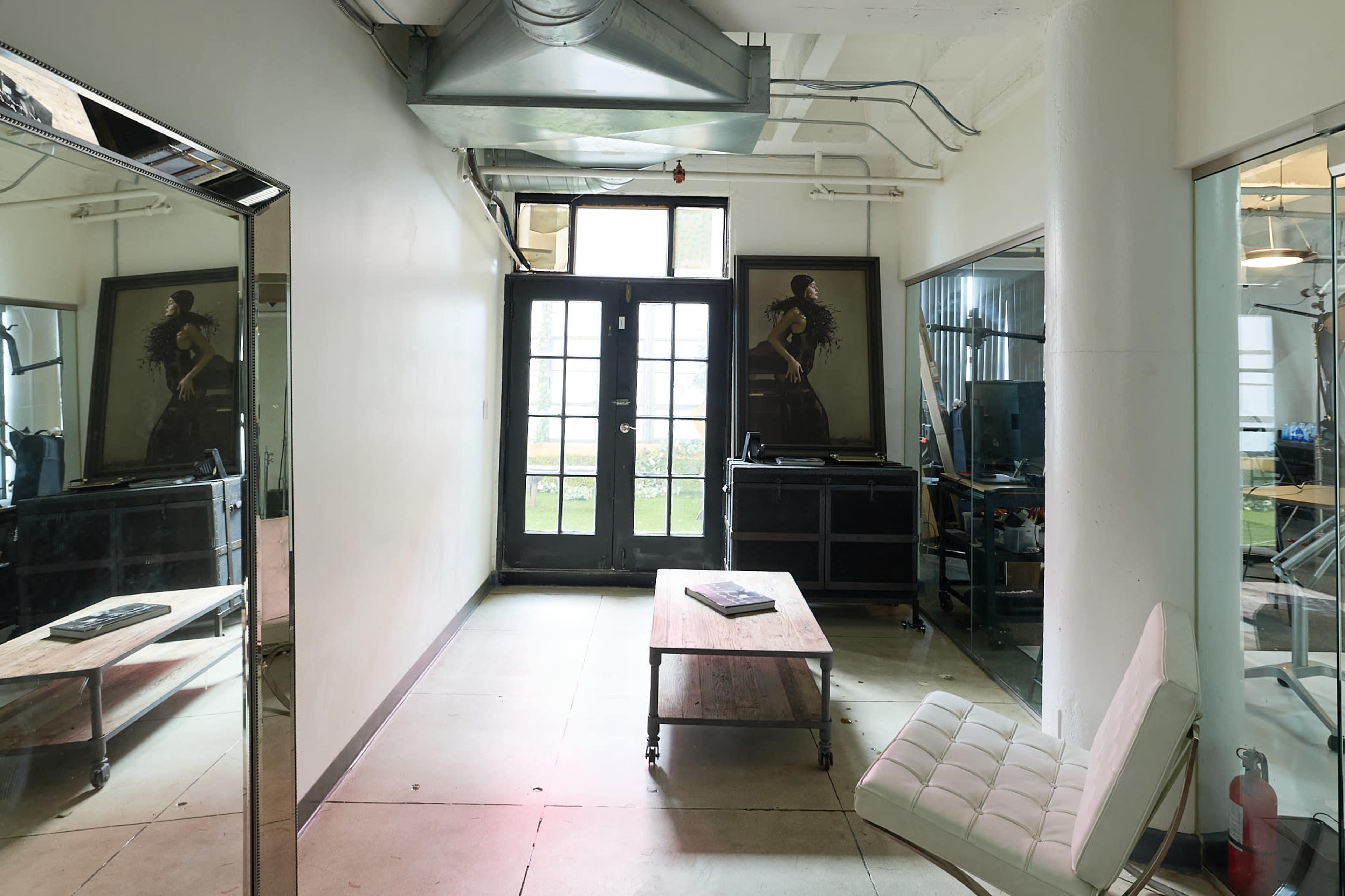The image shows a spacious, modern room with large glass doors leading to an outdoor area, a wooden table in the center, and a stylish chair positioned nearby.