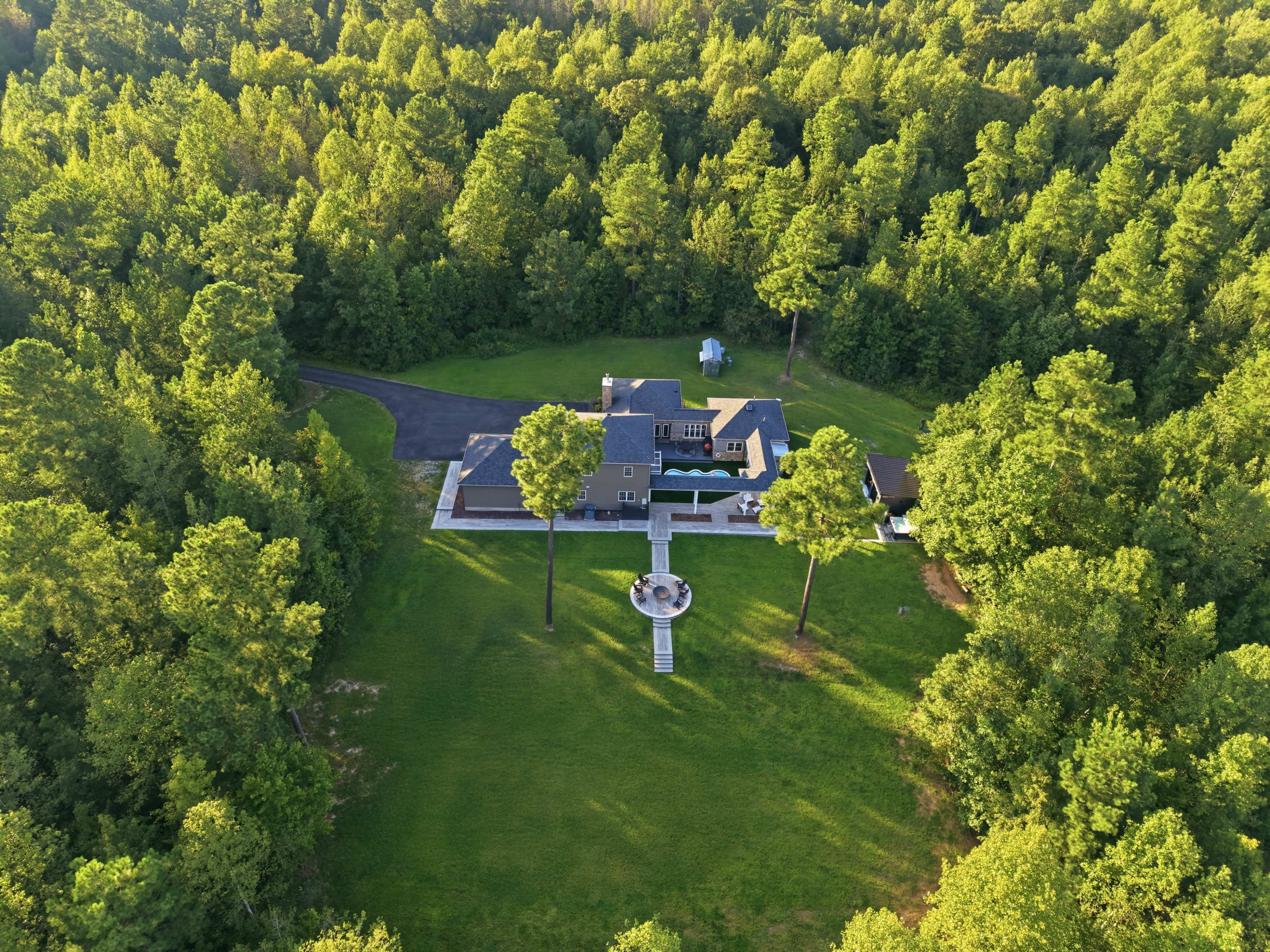 An aerial view shows a large house surrounded by dense greenery, with a circular patio and driveway leading to it.