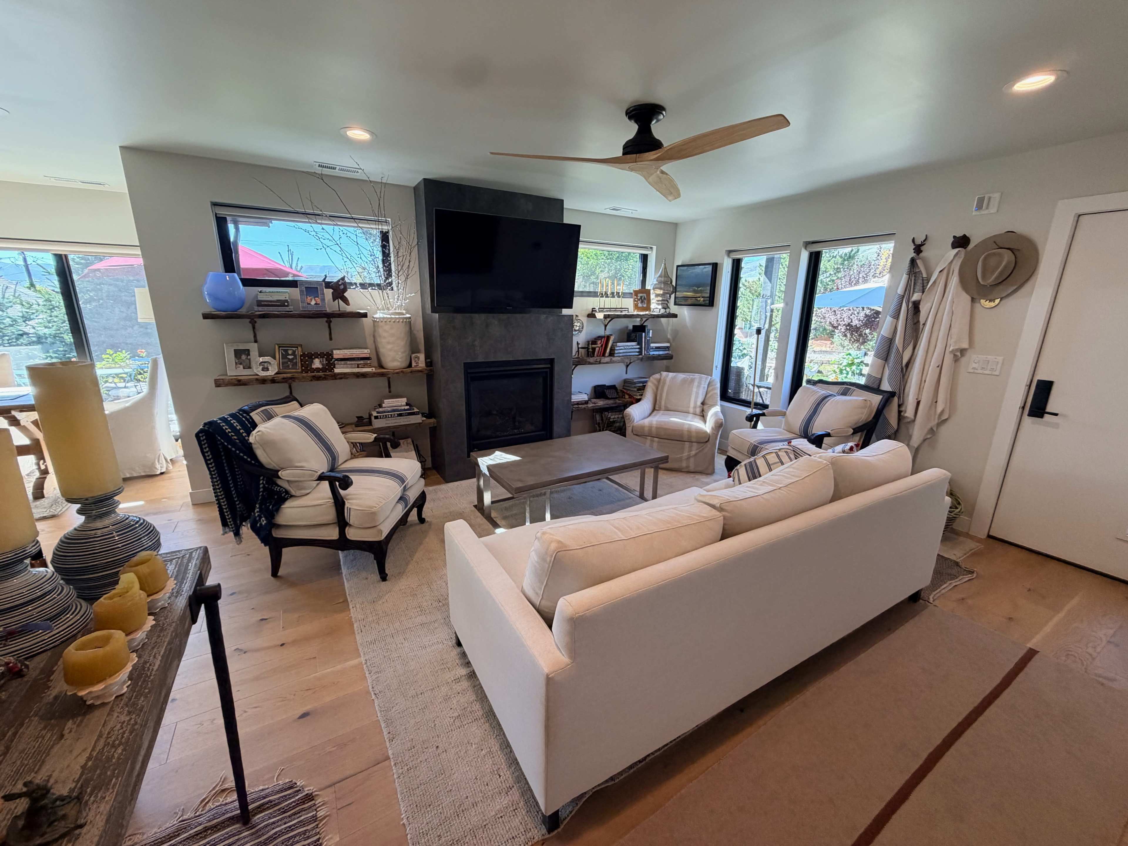 The living room features a modern design with a central fireplace, white sofa, two upholstered chairs, and large windows providing natural light.
