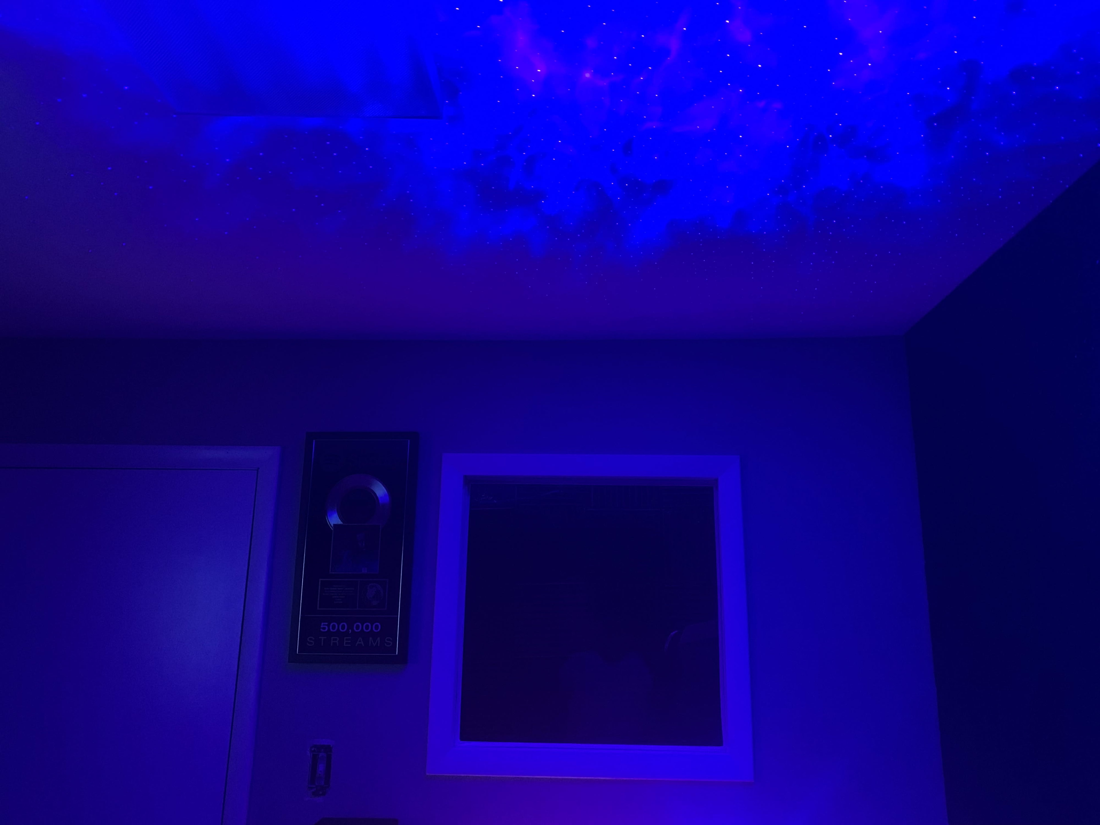 A room with a ceiling illuminated by a starry night sky projection and a framed award on the wall.