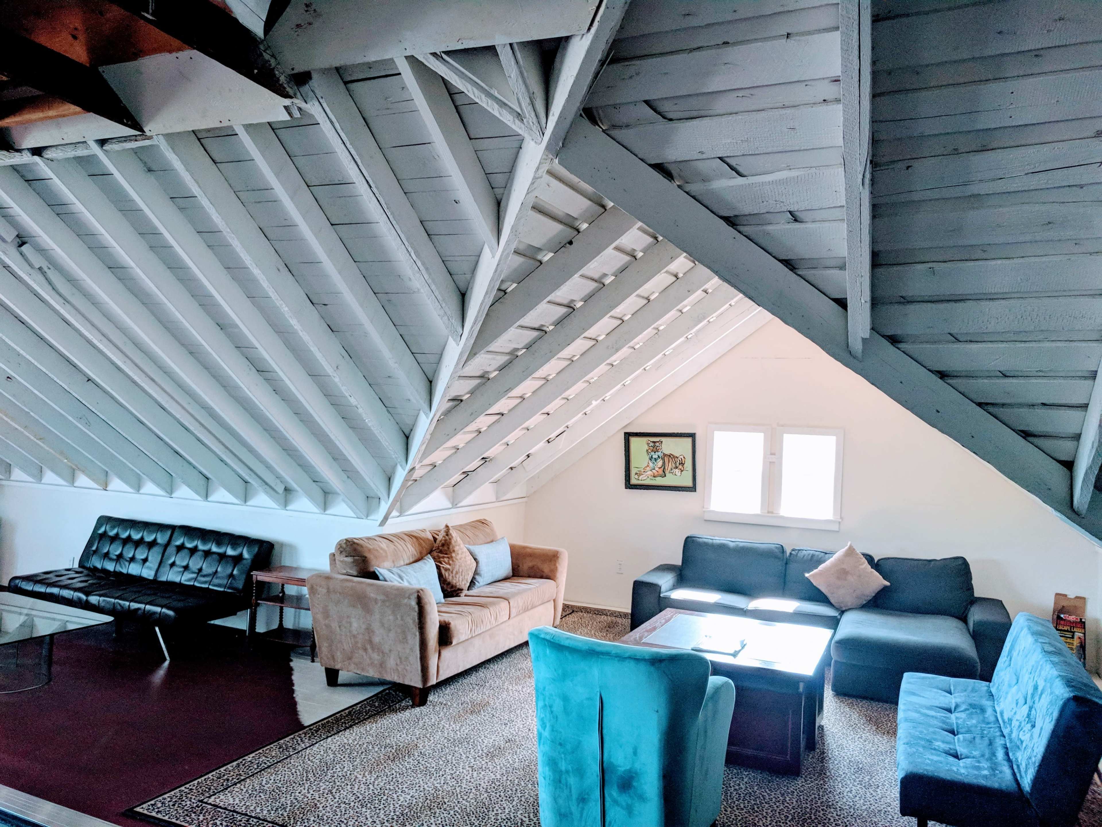 A loft-style living room with slanted wooden ceilings, showcasing a mix of seating options including a brown sofa, gray chairs, and a black futon arranged around a central table.