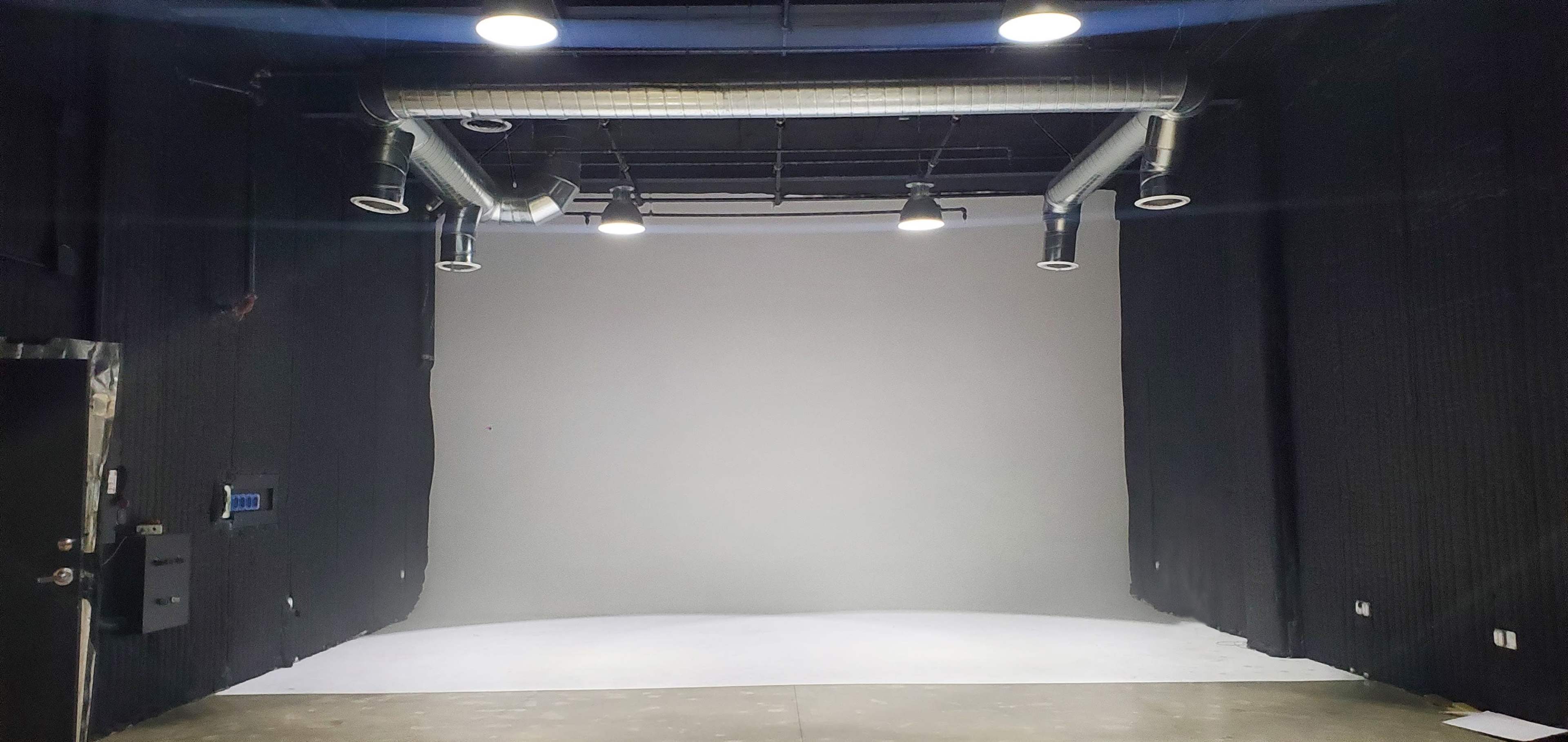 An empty studio space with black curtains, a white curved backdrop, and overhead lighting fixtures.
