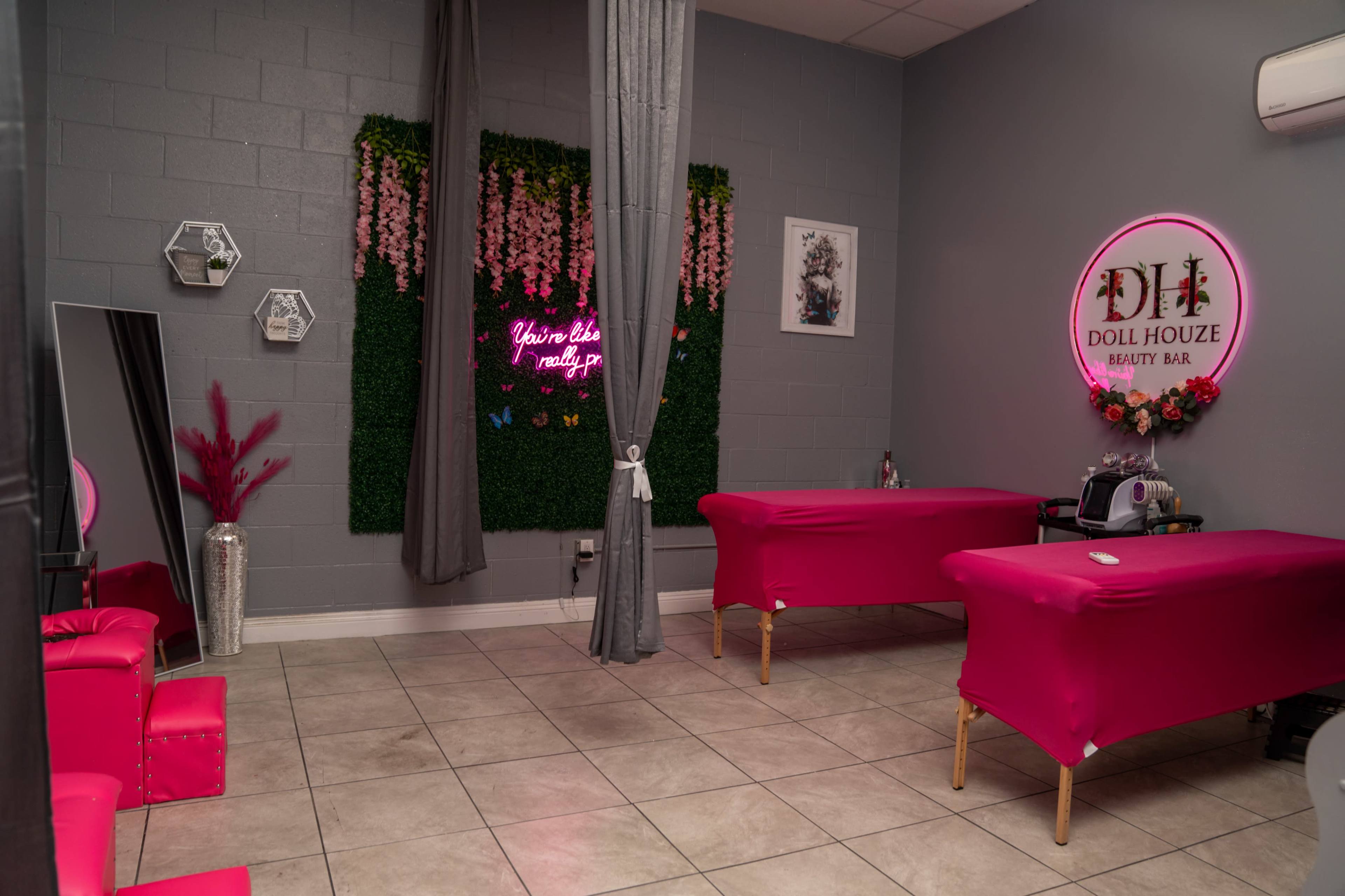 A beauty salon interior with two pink treatment beds, a green wall adorned with artificial flowers, and various decorative elements.