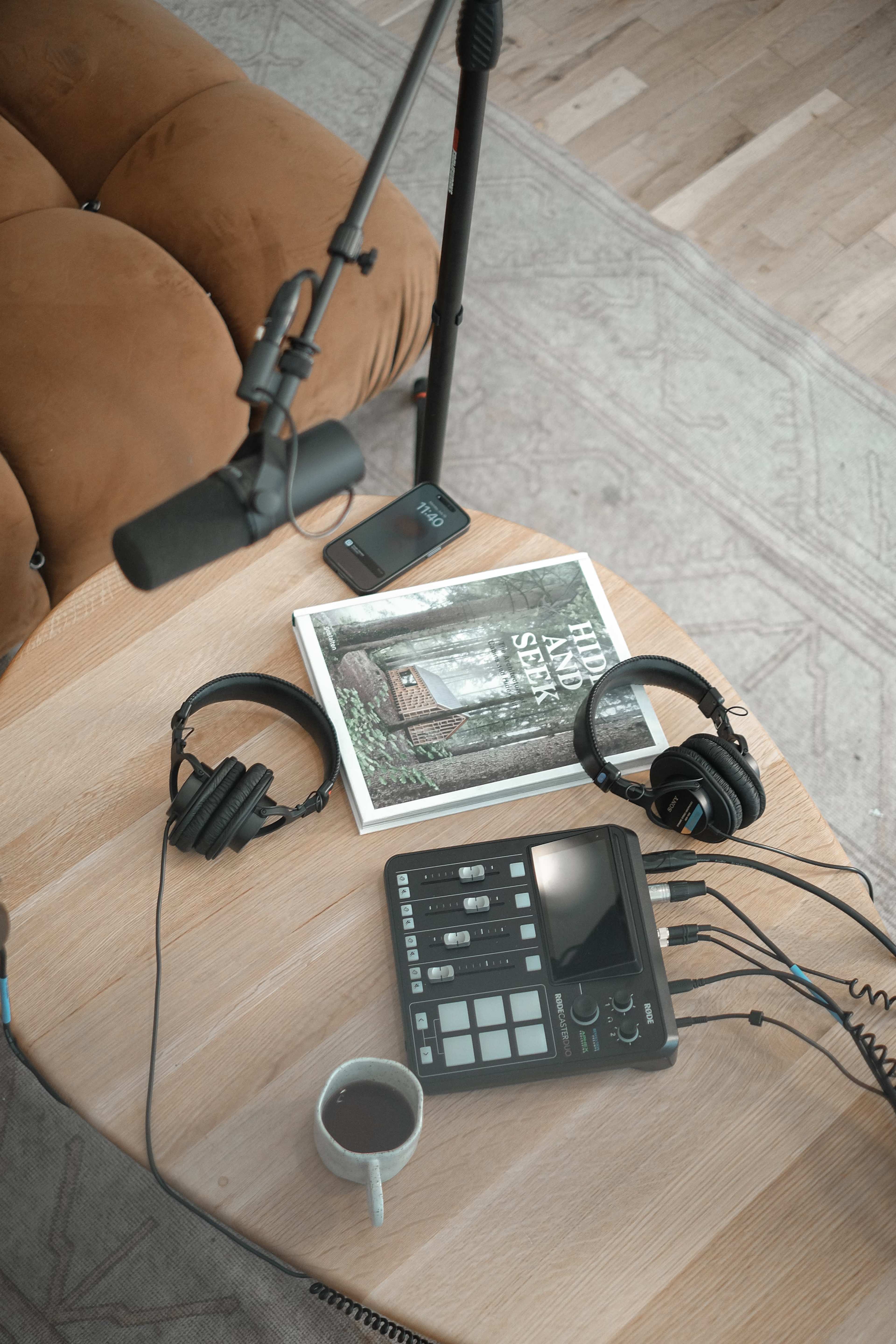 A wooden table holds a coffee mug, headphones, a music production device, a mobile phone, and a book titled "Hard and Soft."