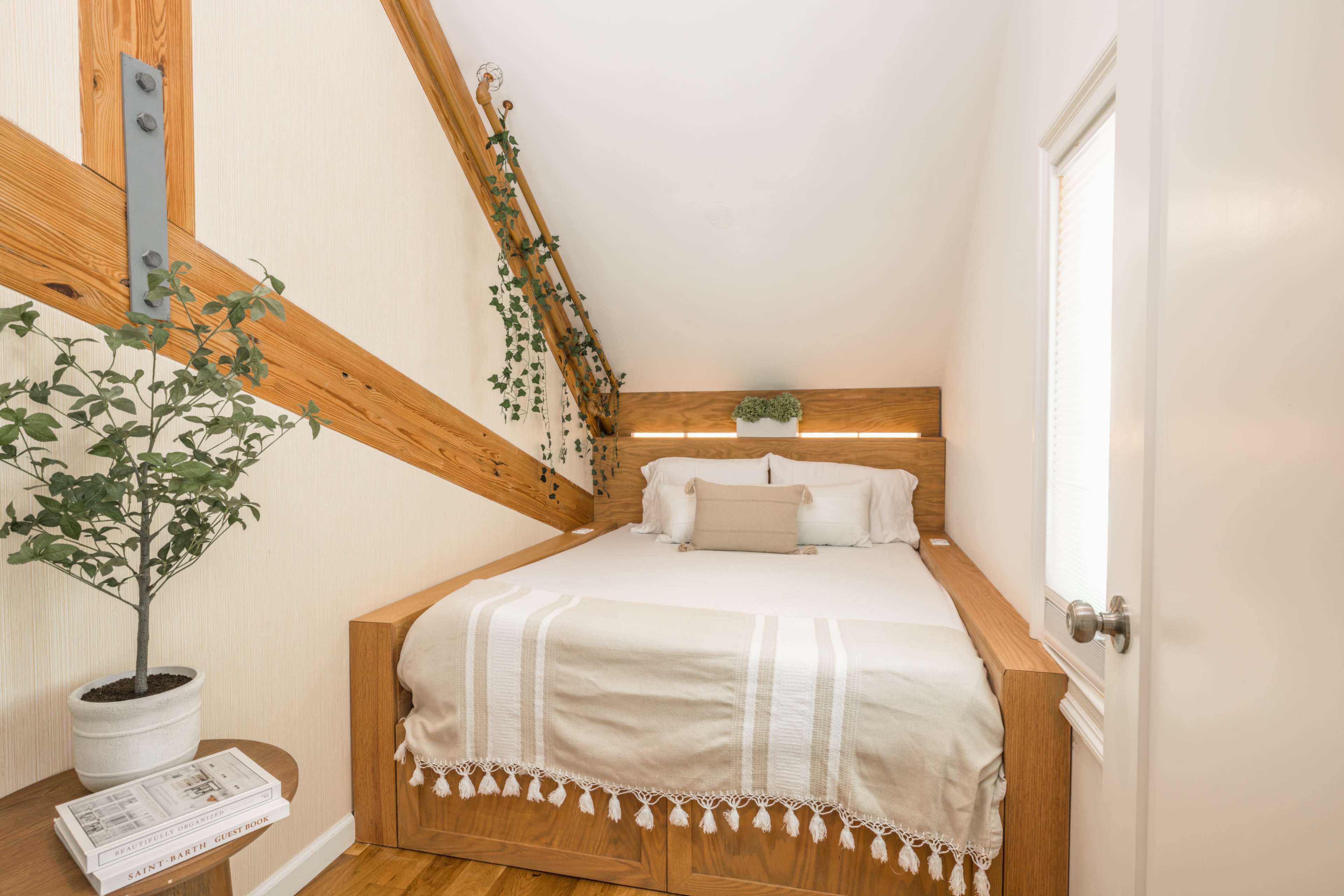 A cozy bedroom with a wooden bed frame, minimalist decor, and a small plant beside the bed.