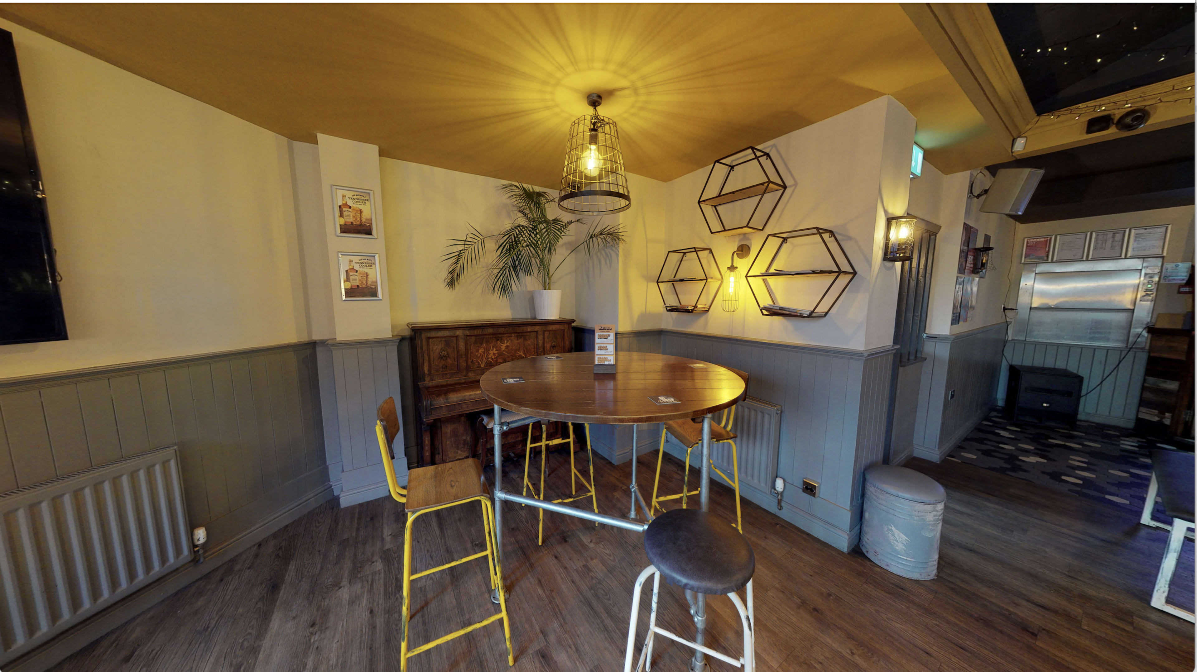 A cozy pub interior with a circular wooden table surrounded by four chairs, a decorative wall planter, and hexagonal shelves.