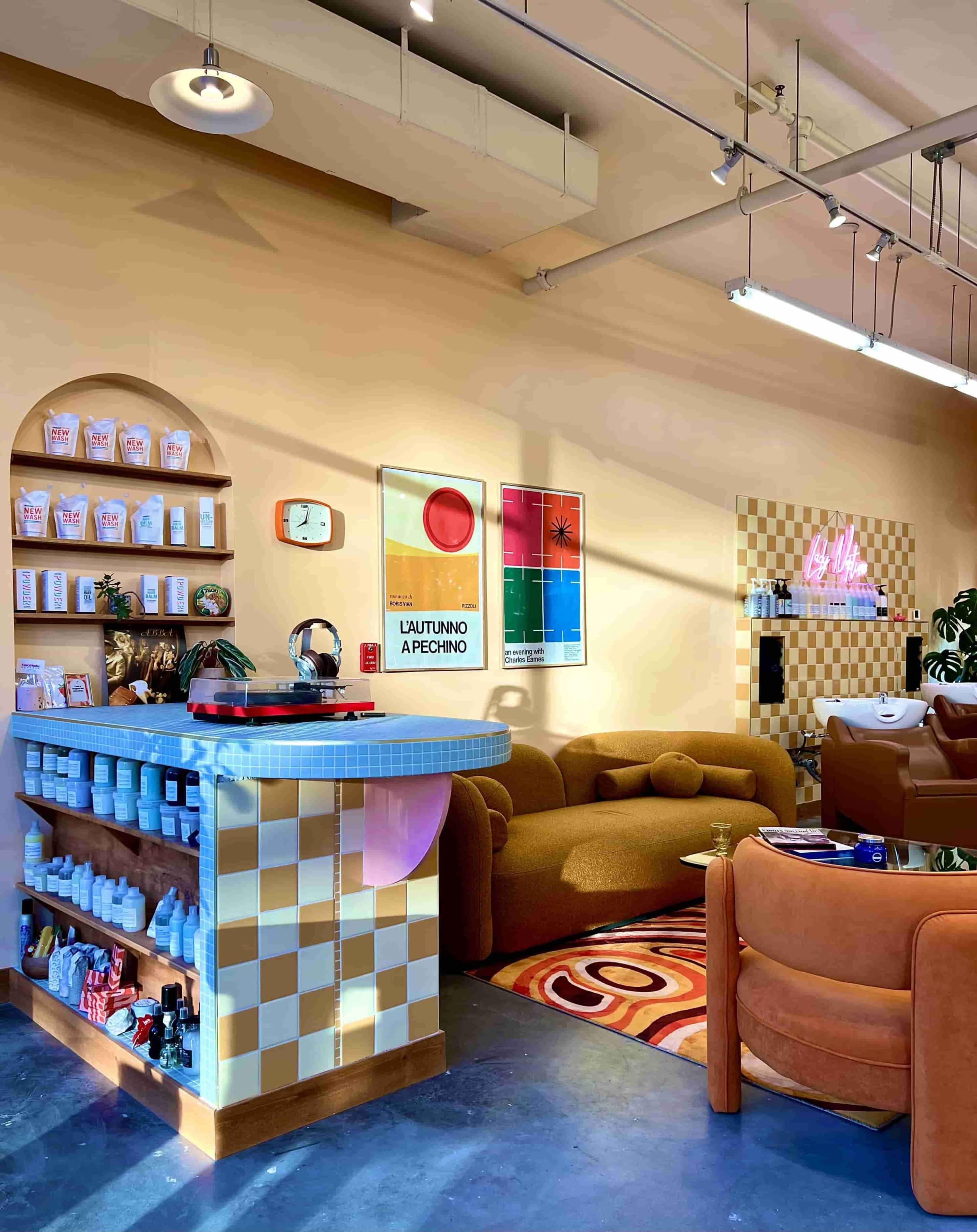 A brightly lit salon interior with a checkered counter, colorful wall art, and cozy seating areas.
