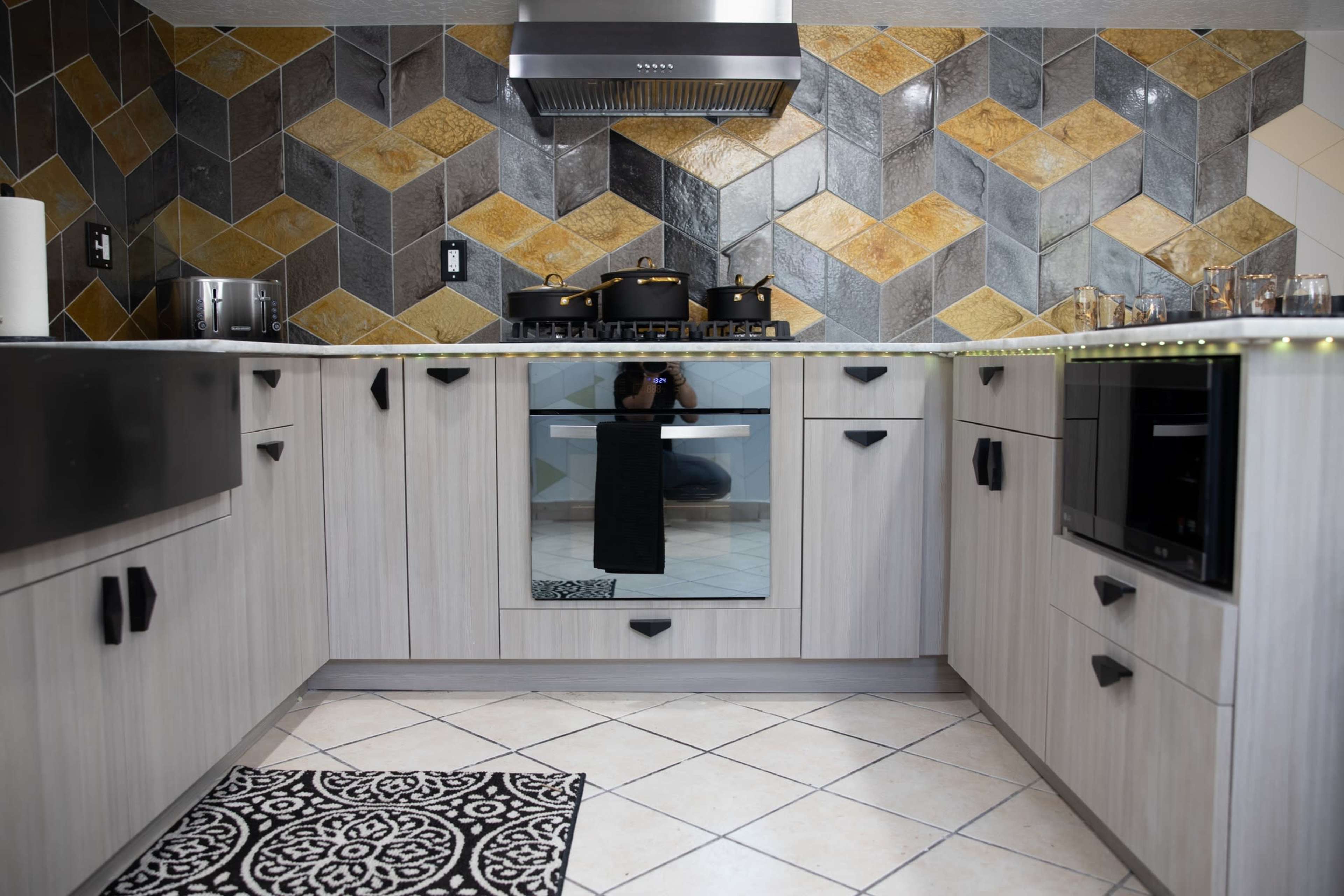 A modern kitchen featuring a herringbone-patterned tile backsplash, sleek cabinetry, and stainless steel appliances.