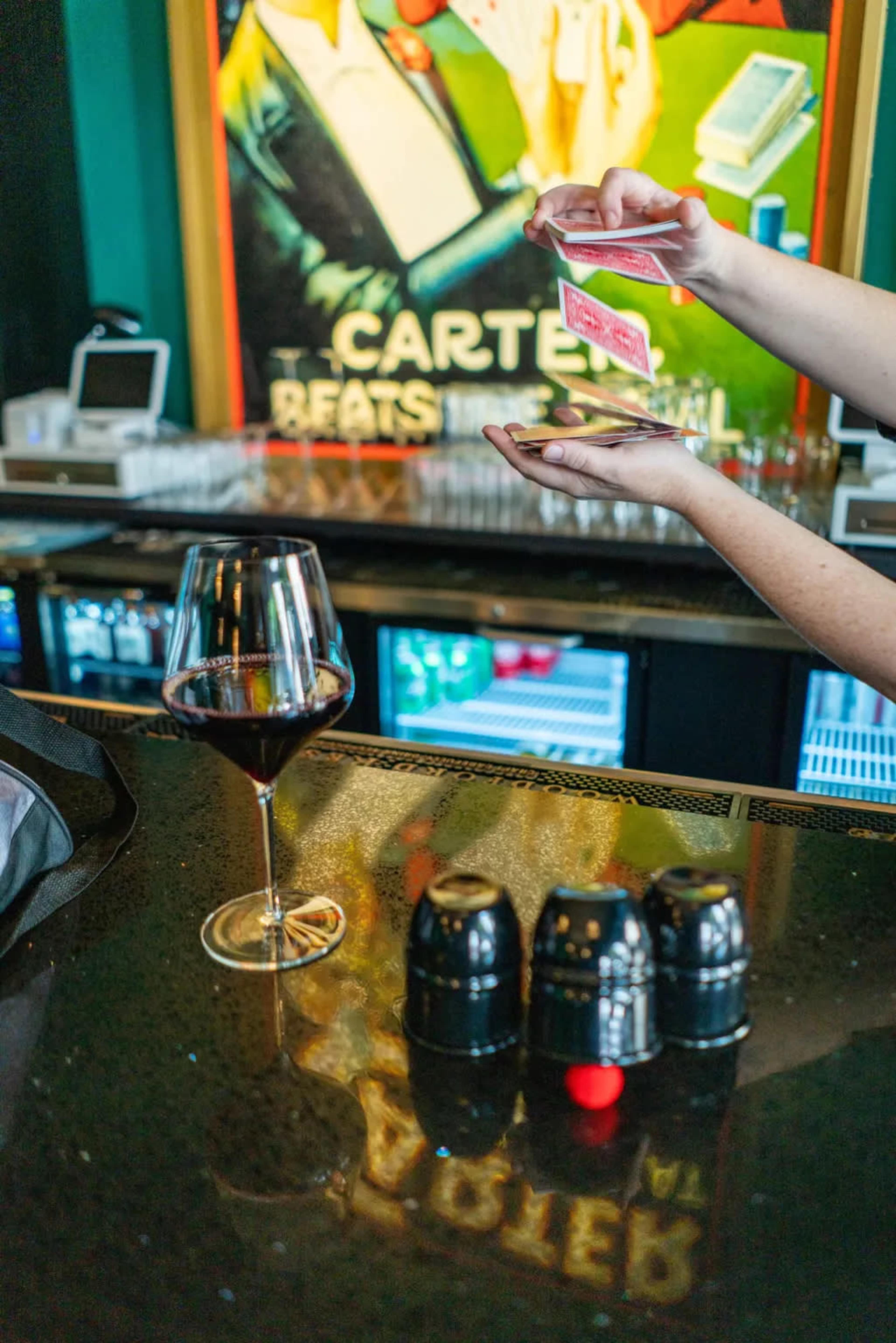 A person performs a card trick at a bar while a glass of red wine sits on the counter.