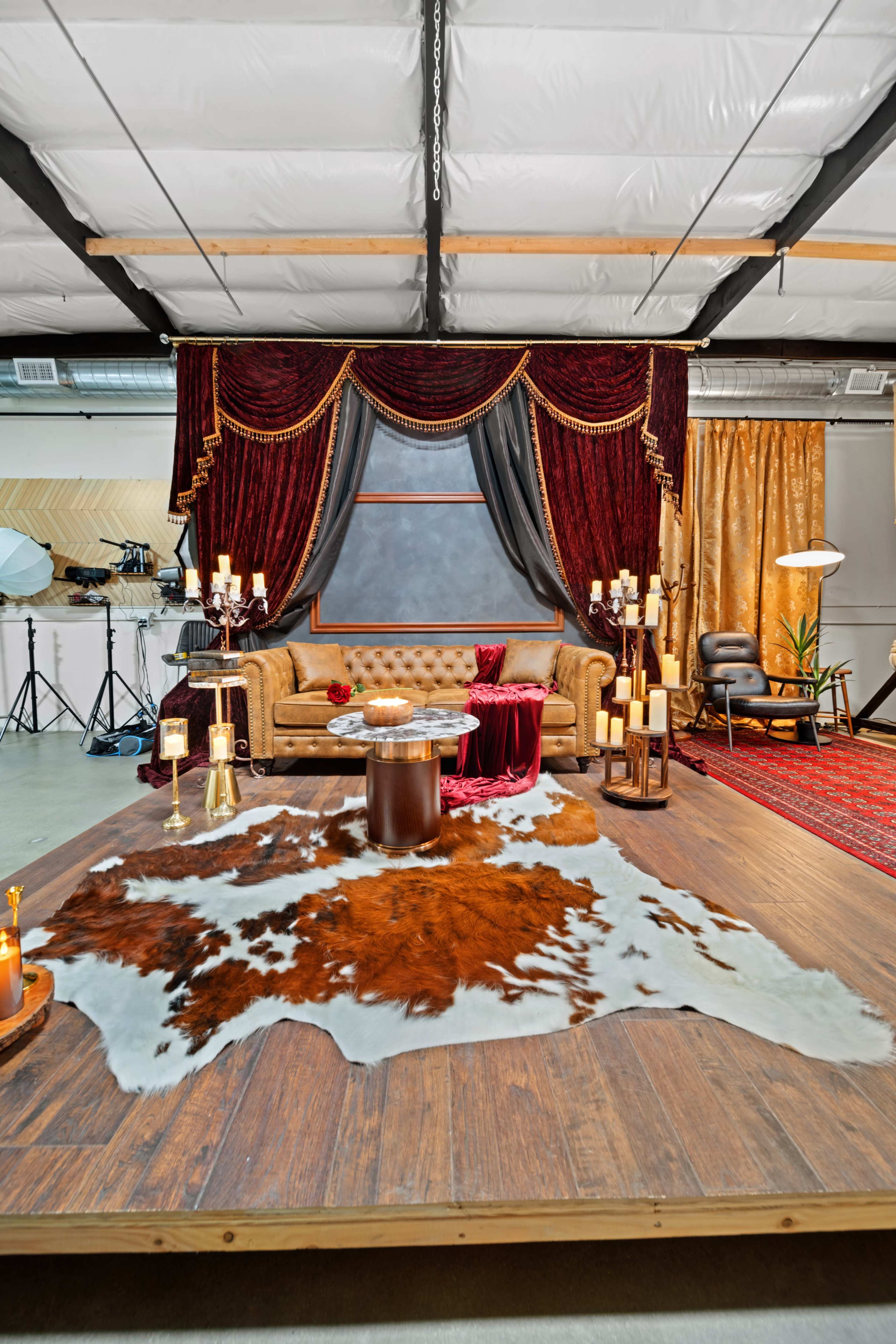 The image shows a stylish interior space featuring a brown couch, a decorative area rug, and elegant lighting, with rich drapes in the background.
