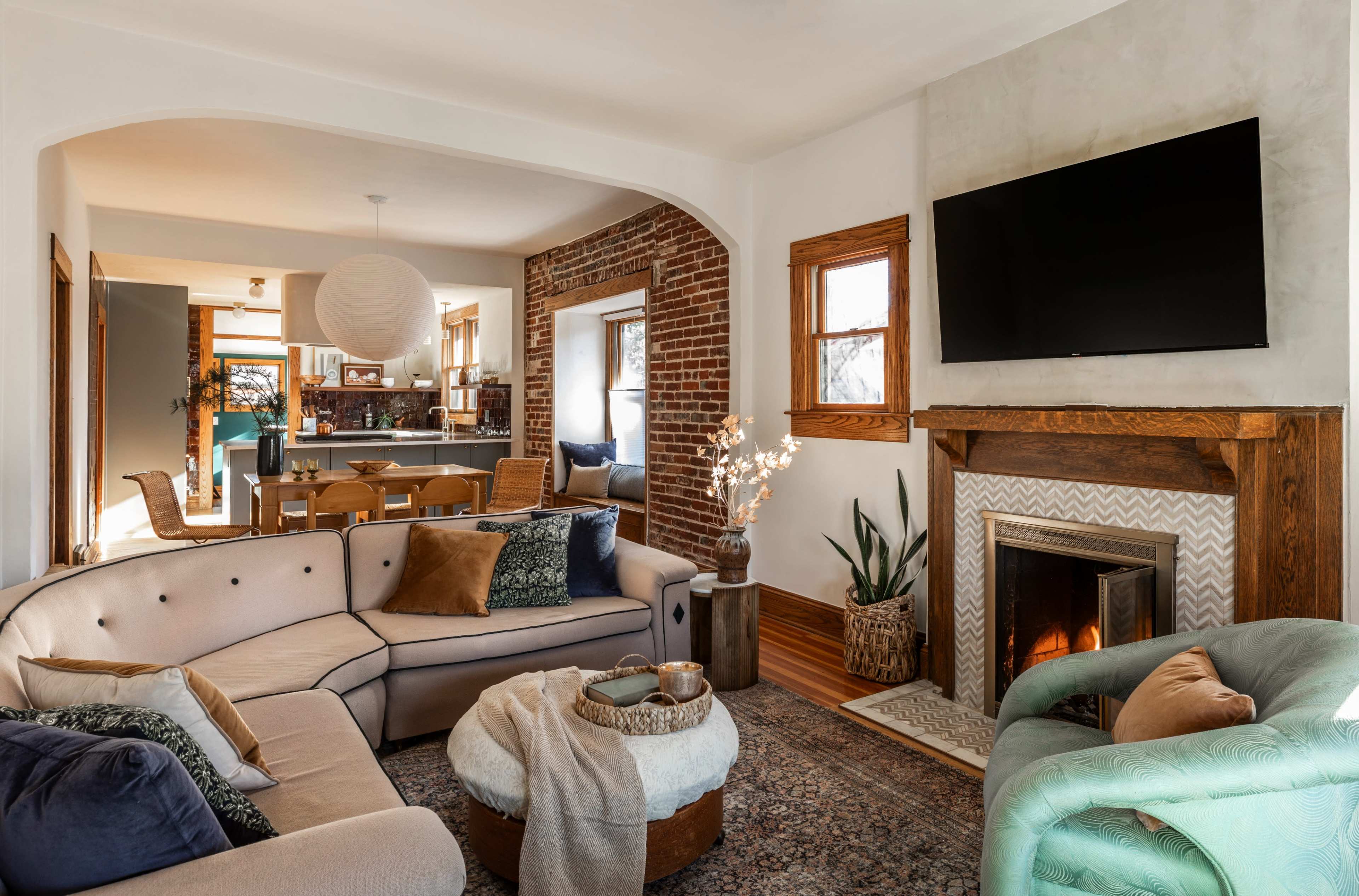A cozy living room featuring a sectional sofa, a round coffee table, and a fireplace, with a dining area visible in the background.
