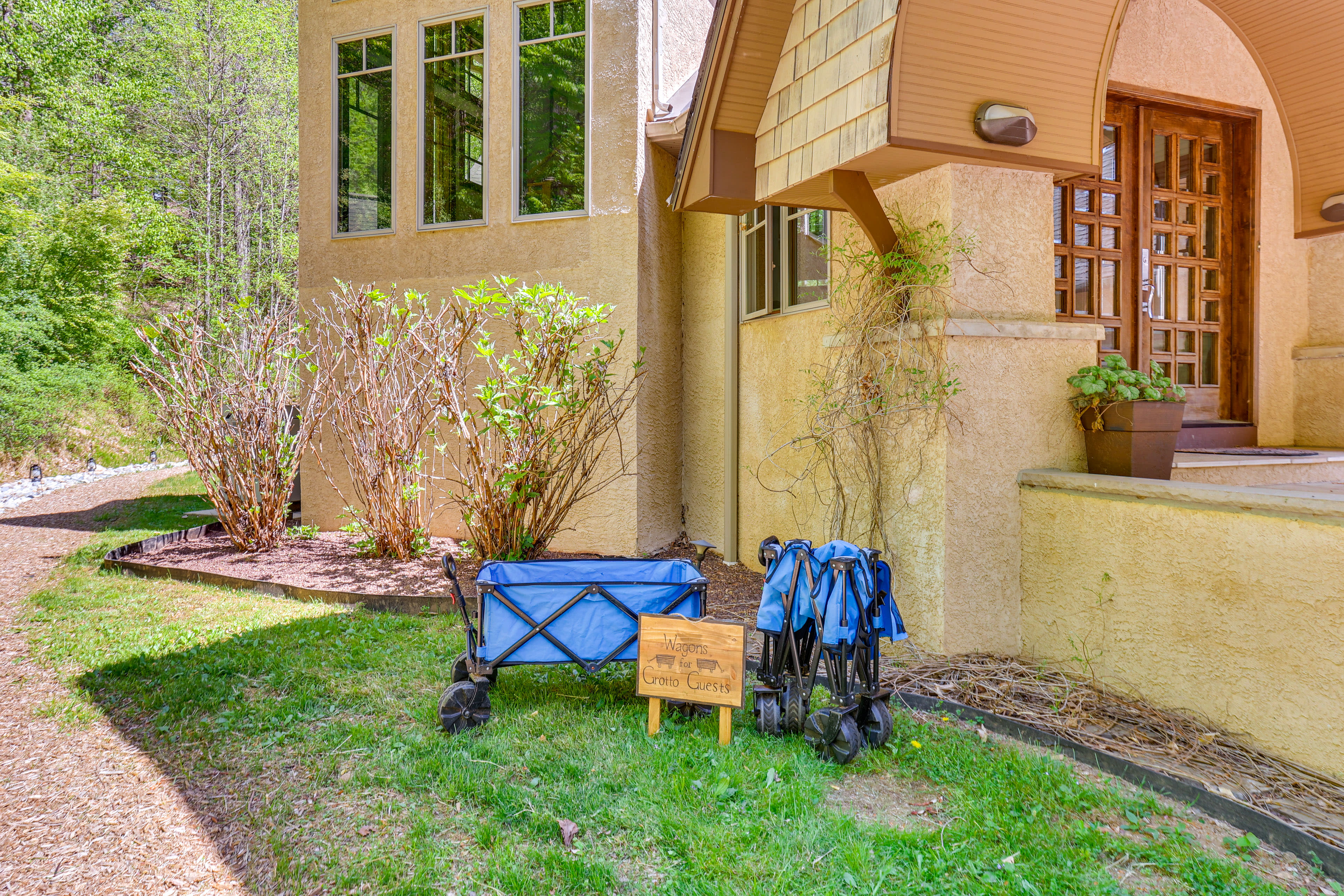 A blue wagon and a sign labeled "United Cabins" are parked next to the side of a beige house surrounded by greenery.