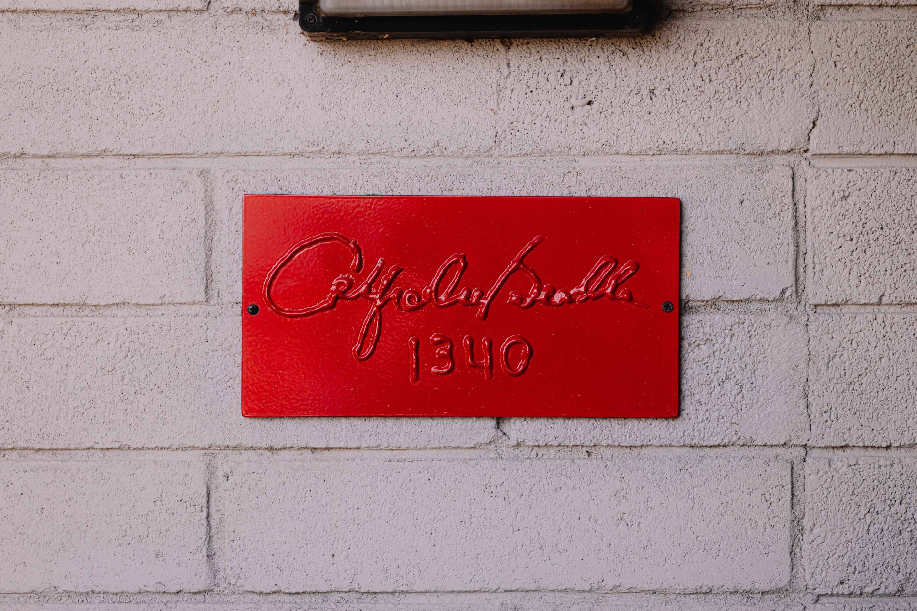 A red plaque with embossed text reading "Café du Monde" and the number "1340" is mounted on a light-colored brick wall.