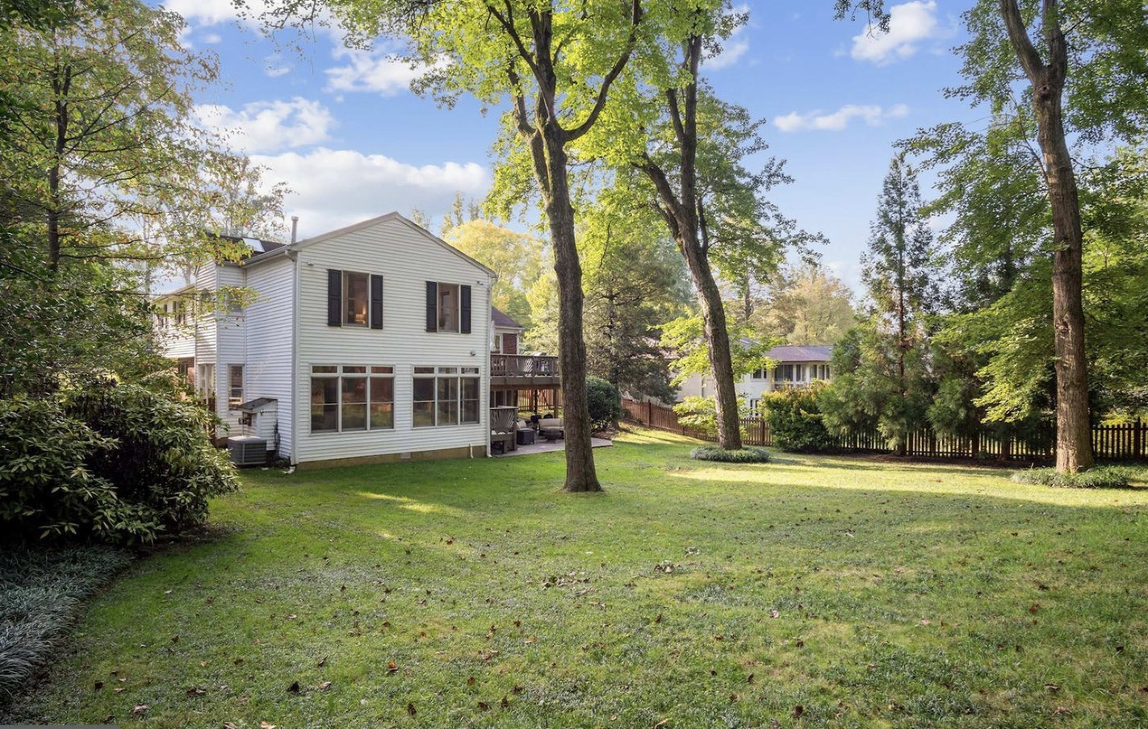 The image shows a white two-story house surrounded by trees and a well-maintained lawn in a residential area.