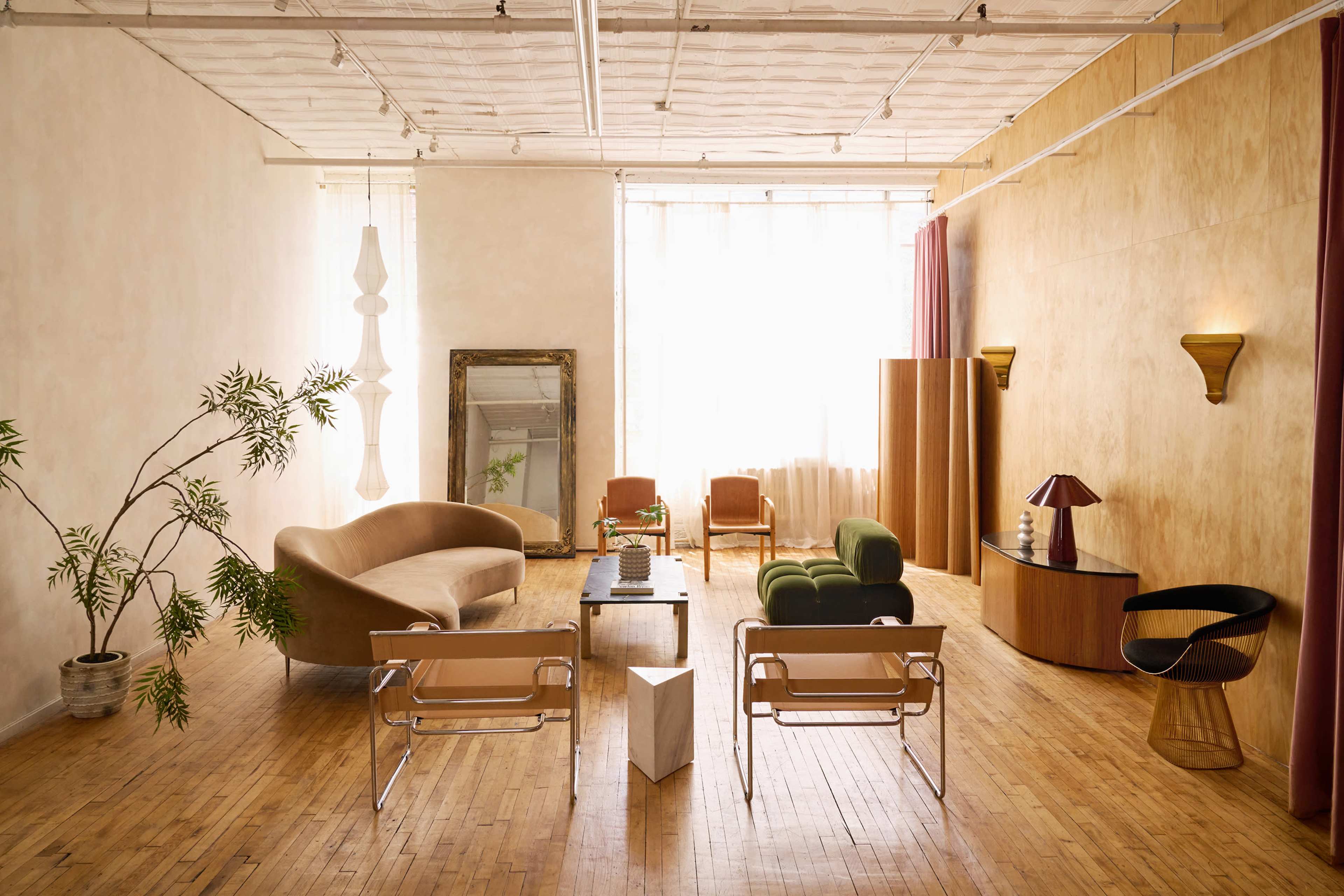 The image depicts a modern living room with a mix of furniture styles, including a curved sofa, minimalist chairs, and a wooden console, arranged around a central coffee table.