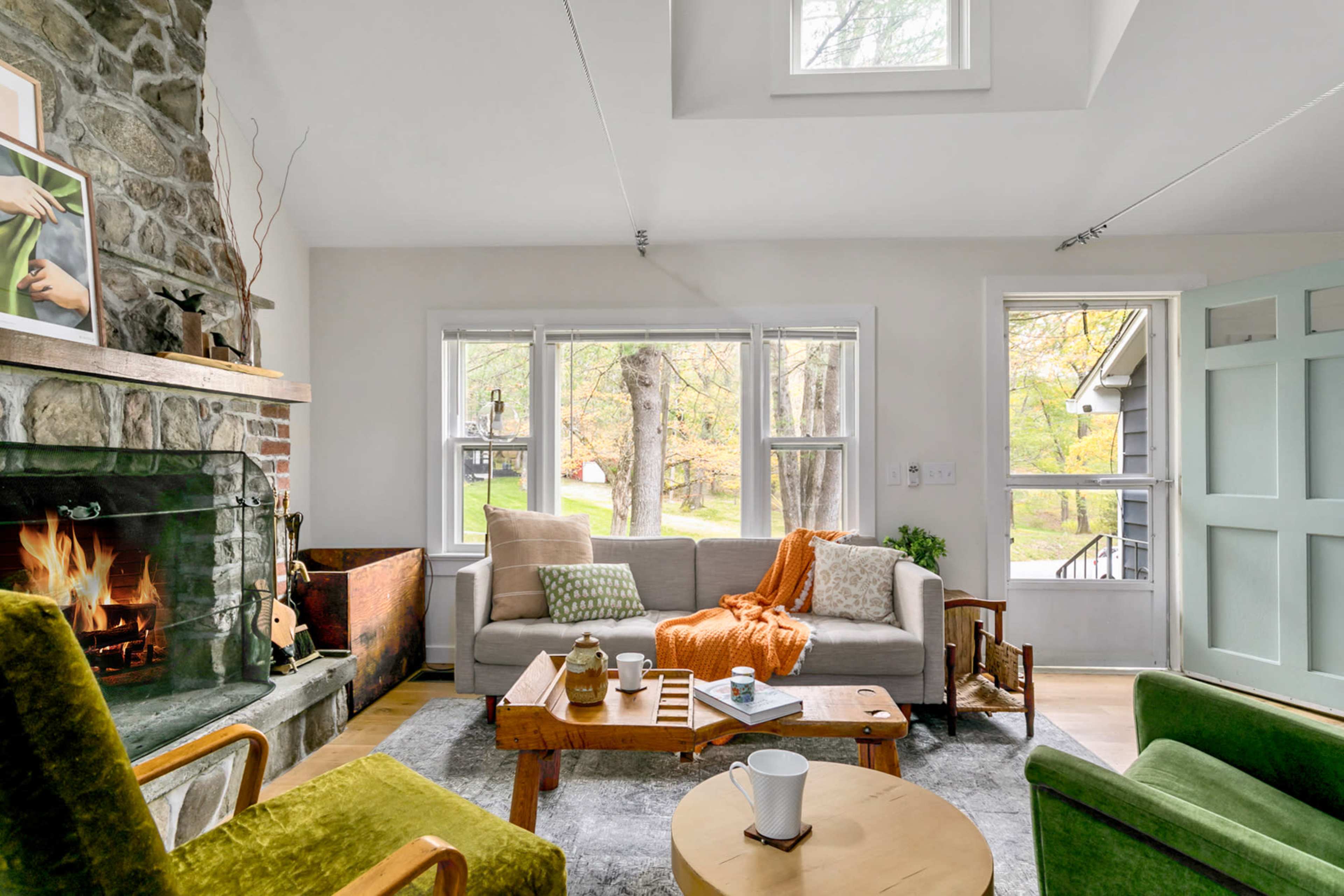 A cozy living room features a stone fireplace, comfortable seating, and large windows overlooking greenery.