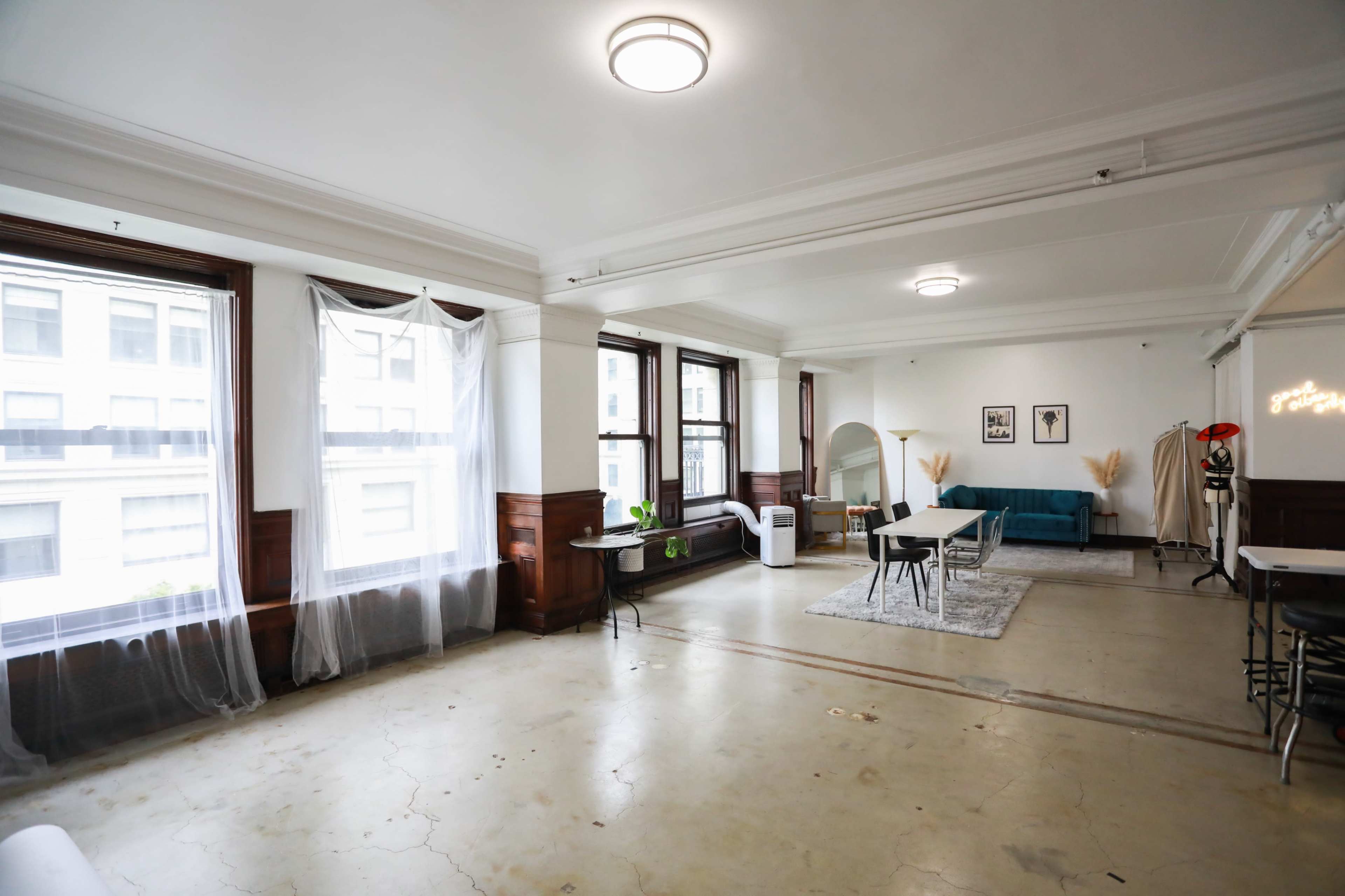 A spacious, well-lit room with large windows, featuring a sofa, a table, and decorative elements.