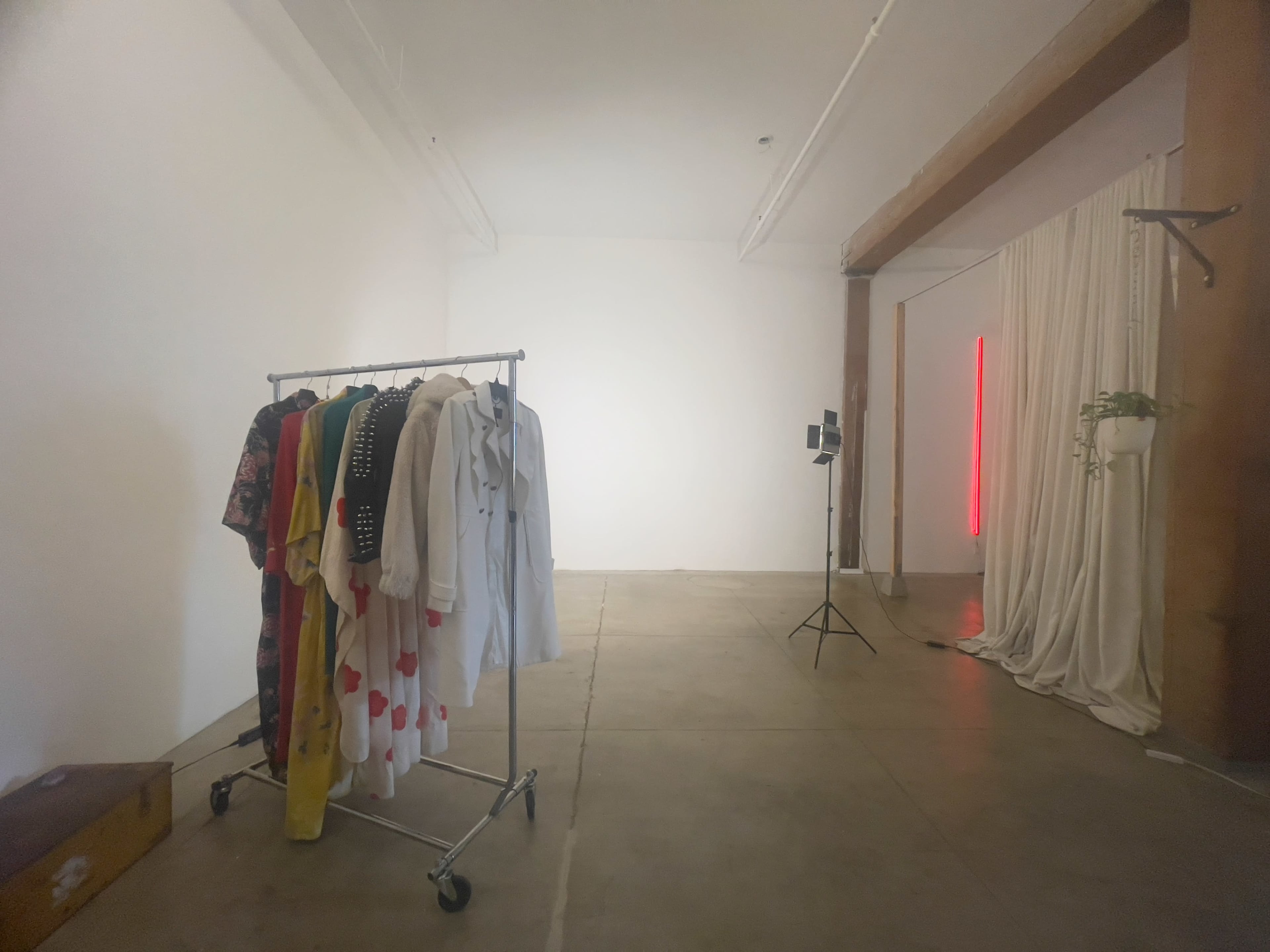 A spacious room with a clothing rack holding various garments, a light stand, and a curtain draped along one wall.